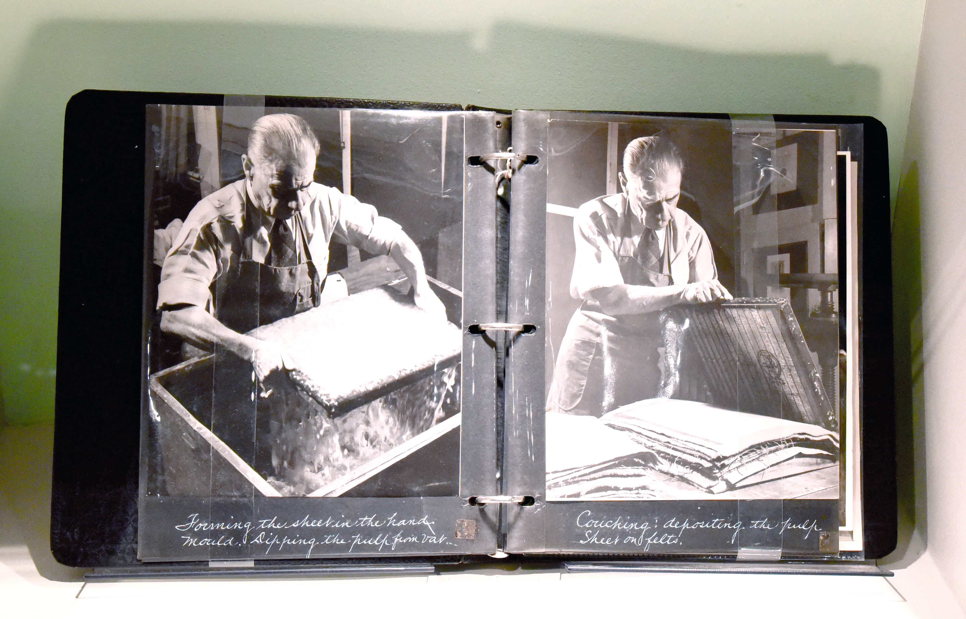 Photo album showing black and white professionally staged photos of Harrison Elliott pulling a sheet of handmade paper and couching it onto felts
