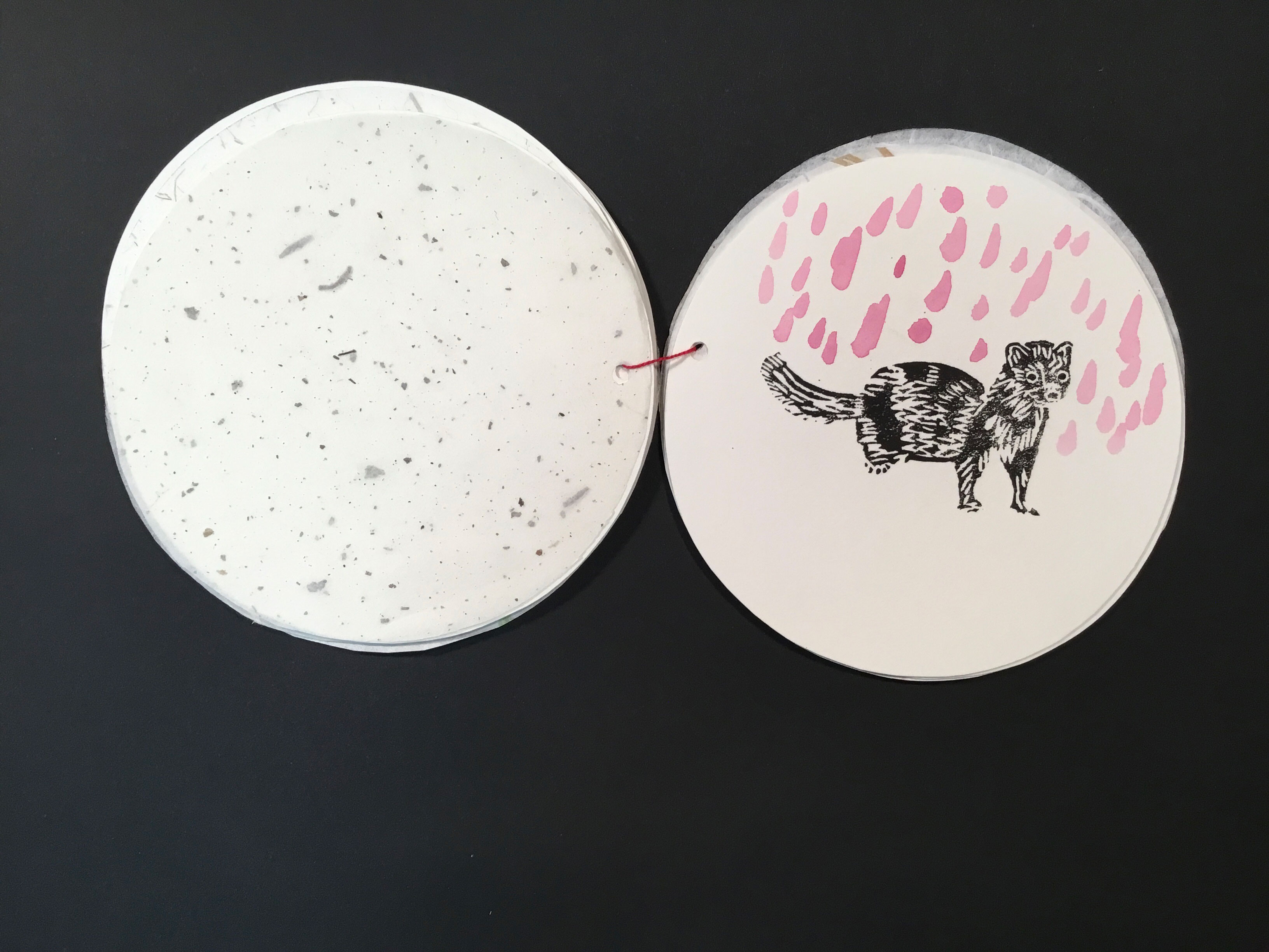 A circular sheet of paper with a painted image of a weasel or ferret on it with pink rain in the background. 