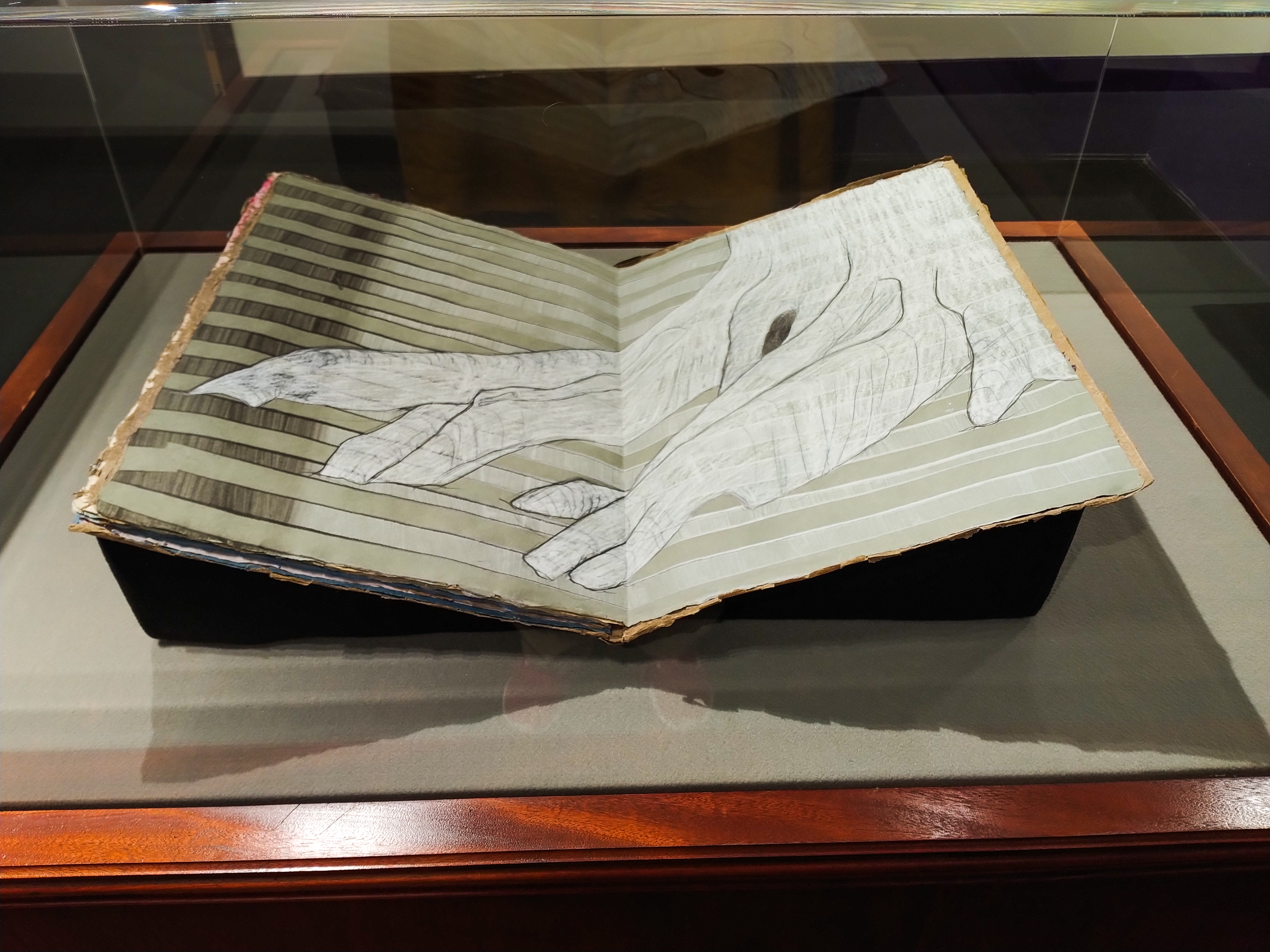 Close up of Union, an artist book by Andrea Peterson. The page on display has white paste painted stripes across the page spread and a white tree painted on top of the lines. Details of the tree are accented with graphite.
