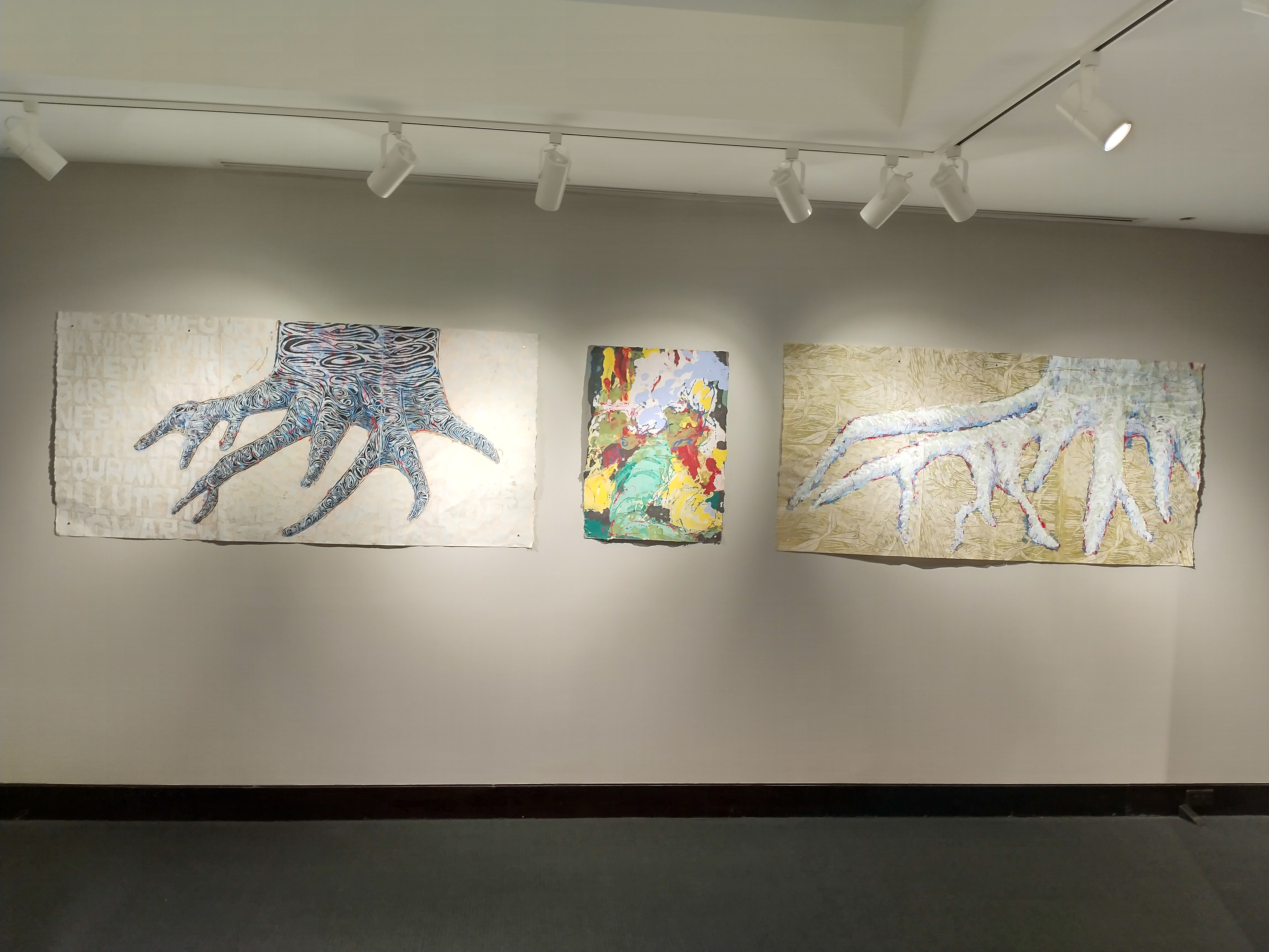 The west wall of the small gallery features two portraits of tree trunks  flanking an abstract piece that are all created by Andrea Peterson. Beech #4 and Beech #2 both combine pulp painting with block prints overtop. Regeneration, the abstract piece has yellow and green shapes that eco the forms of the lower trunk seen in the surrounding work but instead of traveling upwards into a trunk form the upper part of the composition is a swirl of blue, white and yellow.