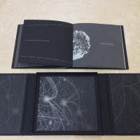 "Strange Constellations" couches black cotton onto bleached abaca to create planets and constellations. Small lines of silvery text are printed on the dark pages of this book.
