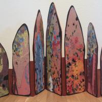 An accordion book with seven house-shaped pages of varying heights ascending from smallest to largest at the center and then descending back to smallest. The pulp paintings mounted on covered boards are connected by a strip of golden brown paper. The pulp paintings speckled sheets that are predominately pink with small bits of black, red, green, and blue. Though the piece is double-sided the image shows only a single view.