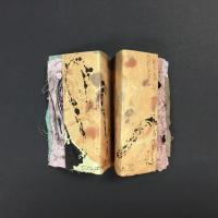 This piece is a folded book with half-sized caramel-colored covers and ink splatters scattered throughout. Each page is a different size, shape, and color, creating the illusion that the book is never-ending.