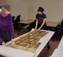 Conservator Stephanie Watkins closely examines a large example of Tapa Cloth, while undergraduate Teresa Munoz assists. 