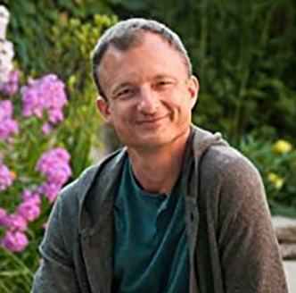Headshot of Book Artist, Shawn Sheehy smiling at the viewer from a garden