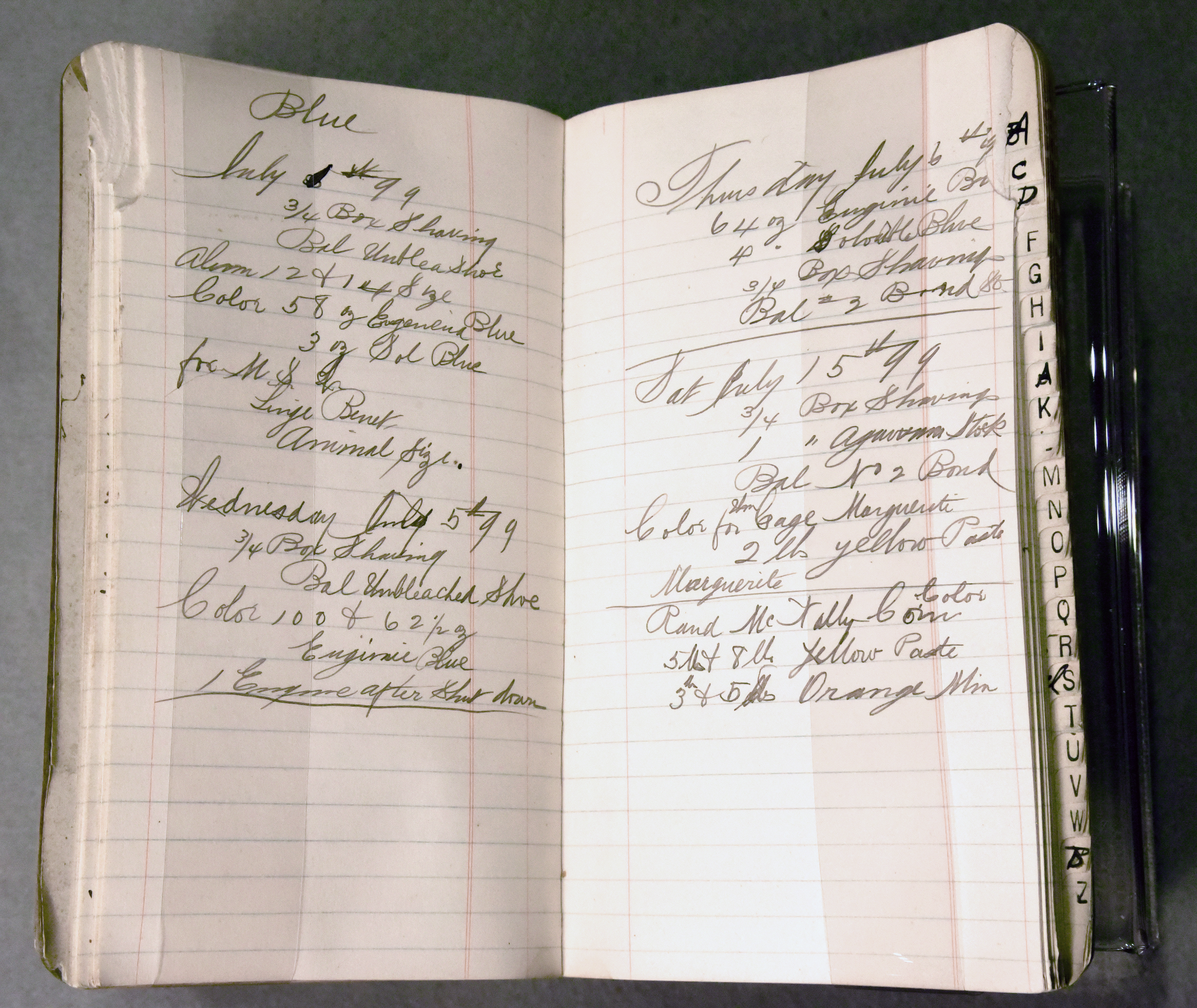 Hardbound book with a notched index from a-z on the right-hand side, book is open showing lined pages with cursive notes about papermaking