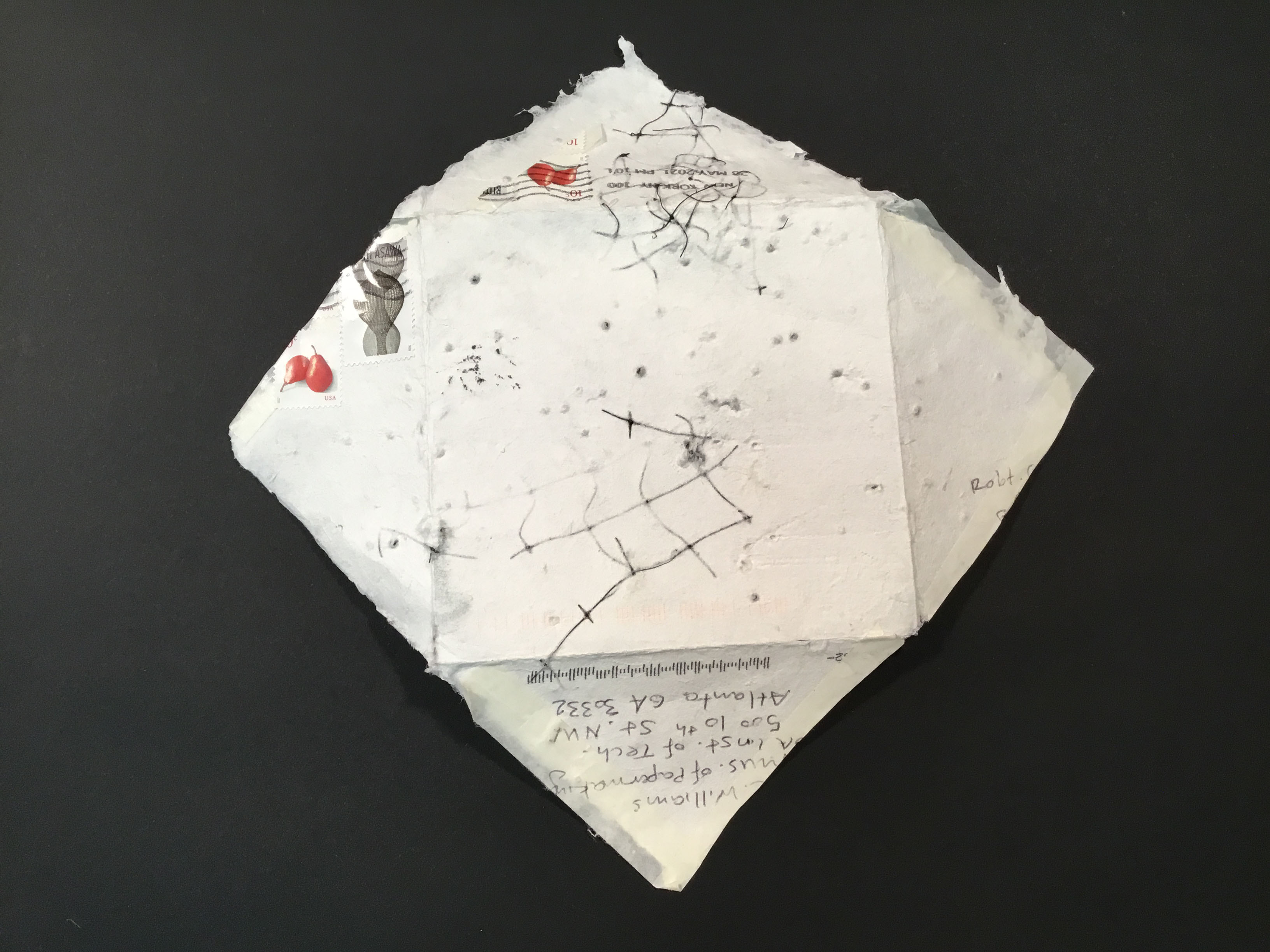A white handmade paper envelope with black beads, bird netting, linen snippets, and black thread as inclusions. The envelope unfolds to become a square sheet of paper.