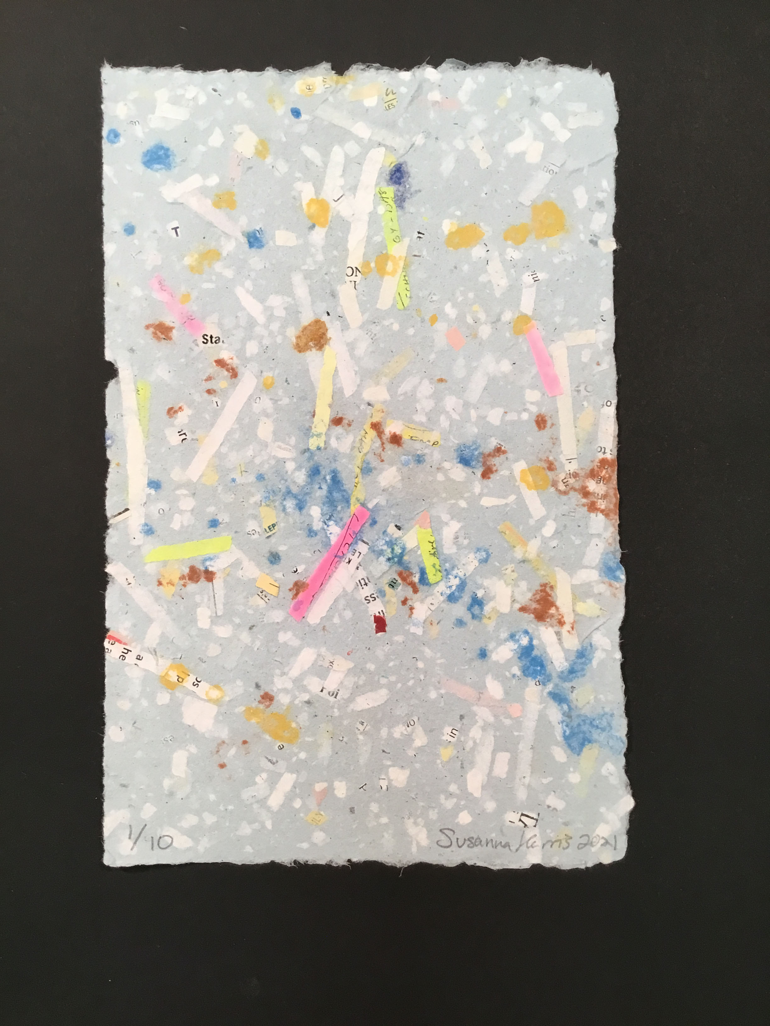  A sheet of light blue-grey handmade paper with blue, orange, and rust-colored lint, pink, green, and white office paper, and deckled edges.