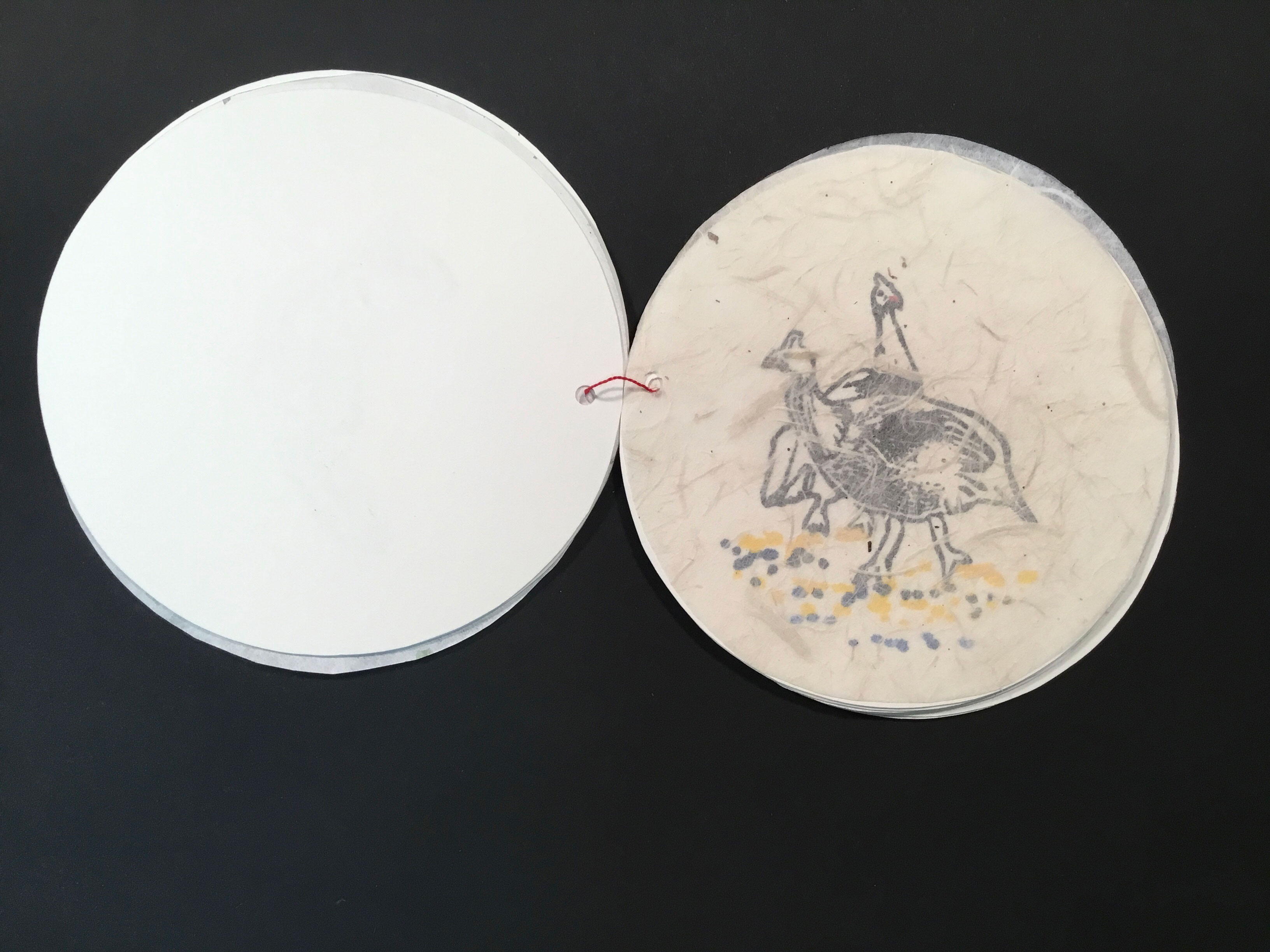 A thin, circular sheet of translucent paper with floral and plant-like embeds covers a painted image of two wild turkeys standing on yellow and black dots.