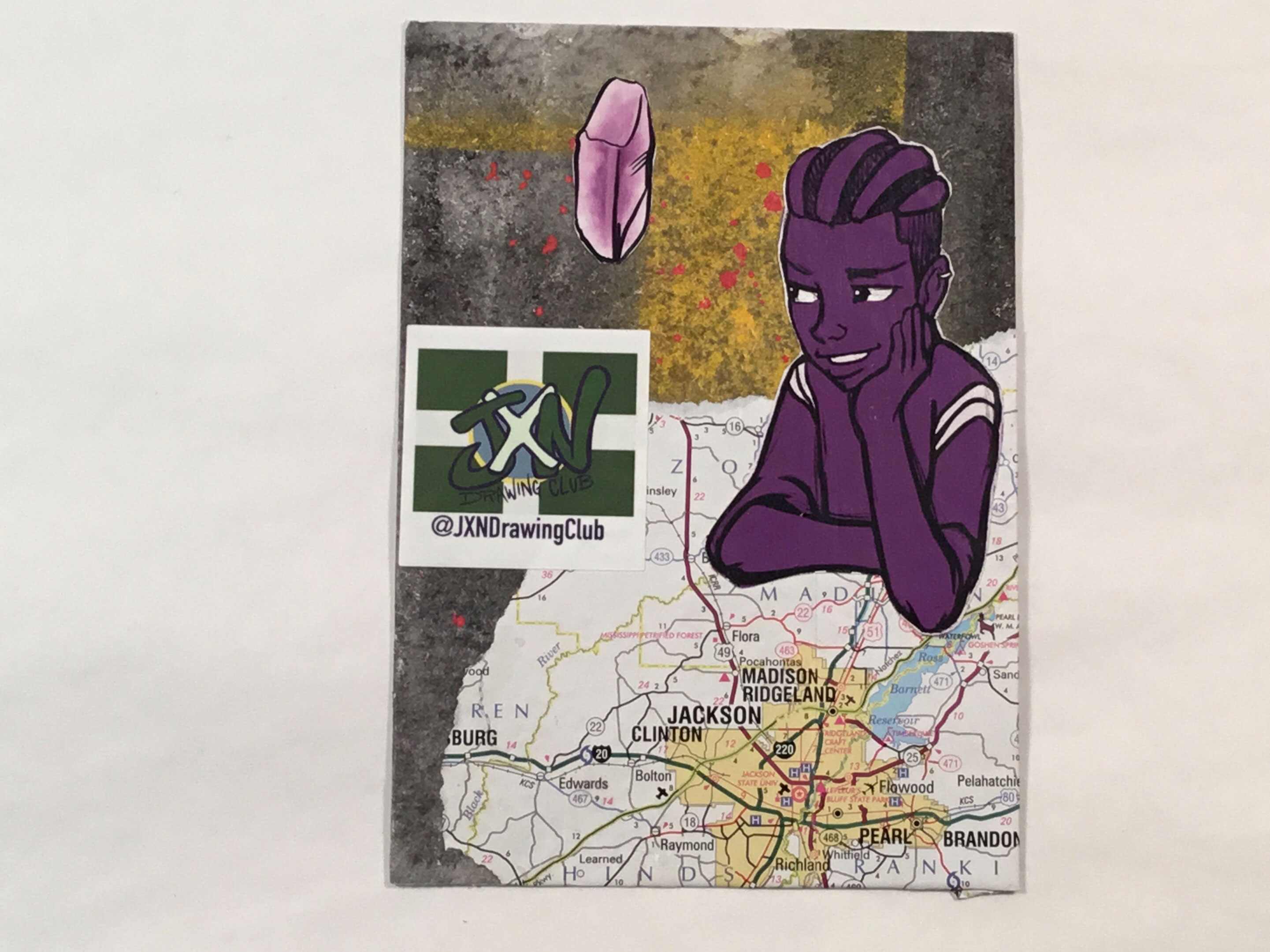 A purple illustration of a young African American man sits atop a torn section of a map depicting Jackson, Mississippi. In the background is a gray and yellow paper with red paint splatters on top, as well as a light purple illustration of a crystal in the top left corner.