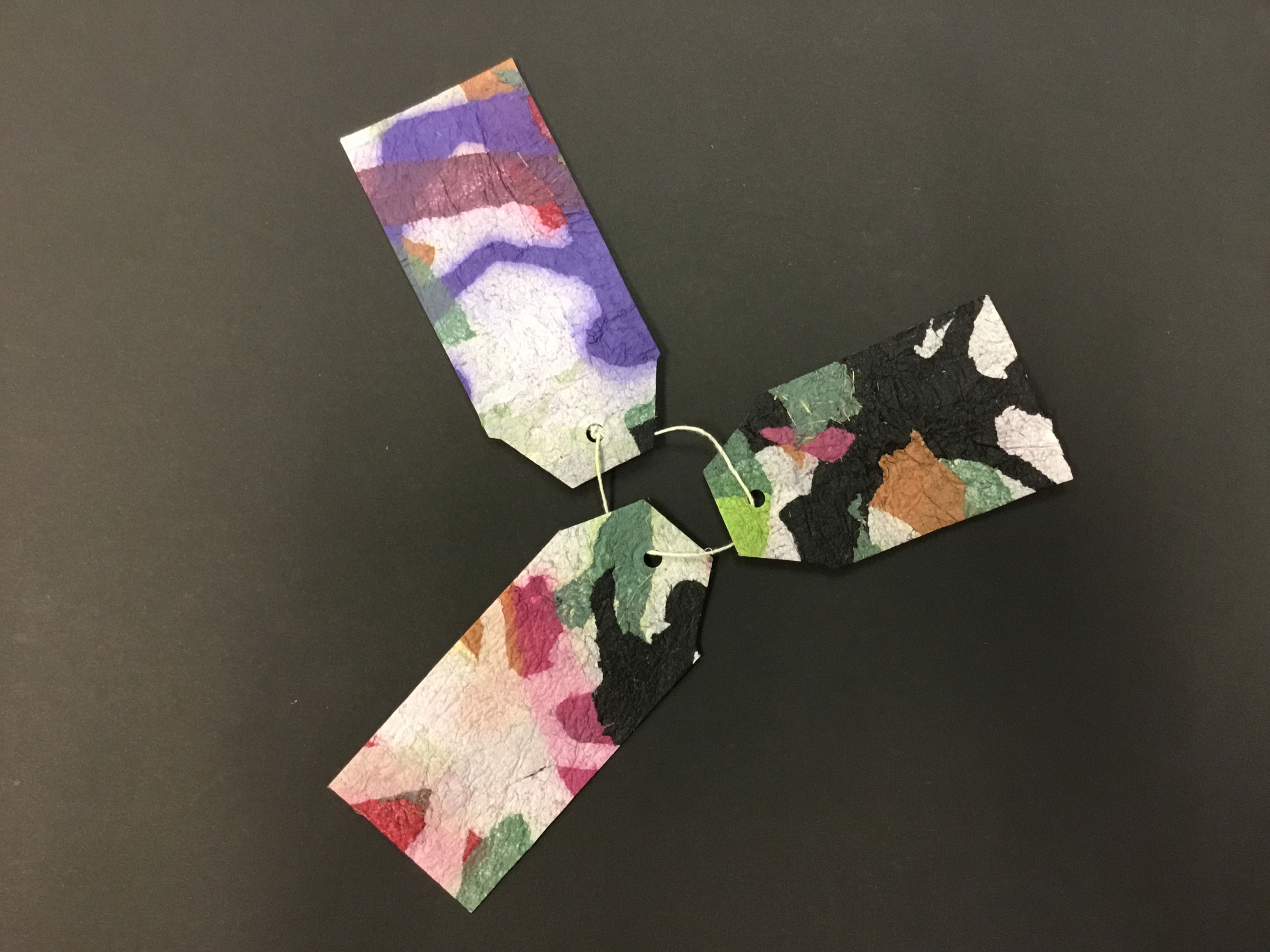 This piece is comprised of three handmade paper “tags” made from the Korean technique known as “joomchi” and created from mulberry paper. The tags are a variety of colors, including purple, blue, green, pink, brown, and white. According to the artist, the illustrations are meant to portray people and abstract suburban landscapes.