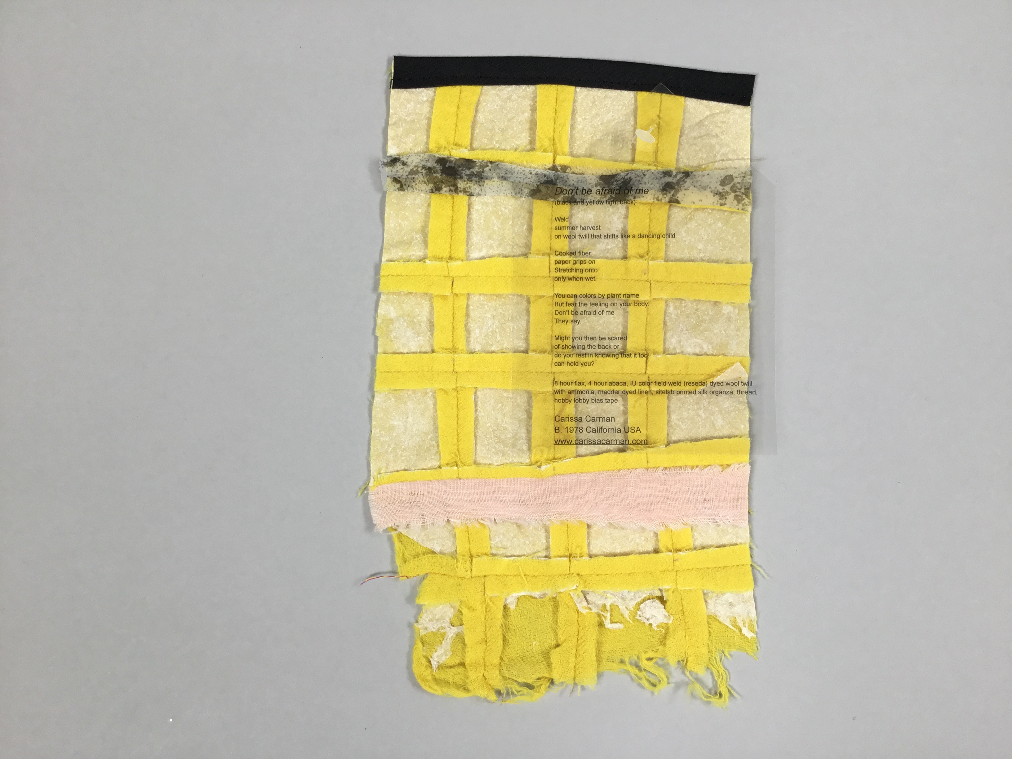 This piece, entitled “Don’t Be Afraid of Me”, is a yellow and beige quilted rectangle made of fabric scraps. The right side of the piece has a translucent sheet with a poem printed onto it.