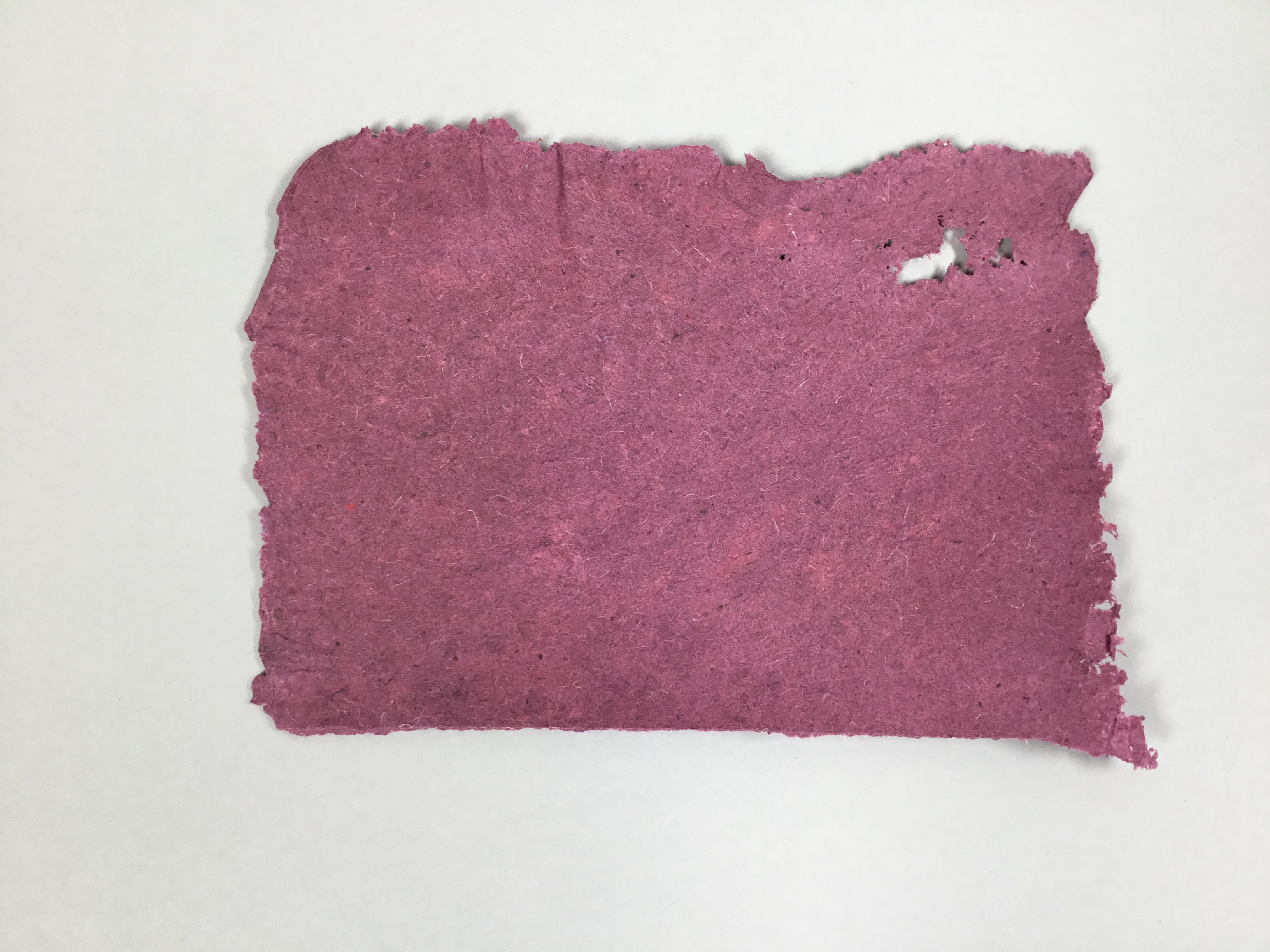 This piece is a mulberry-colored sheet of square, handmade paper with raw edges and visible fiber threads.