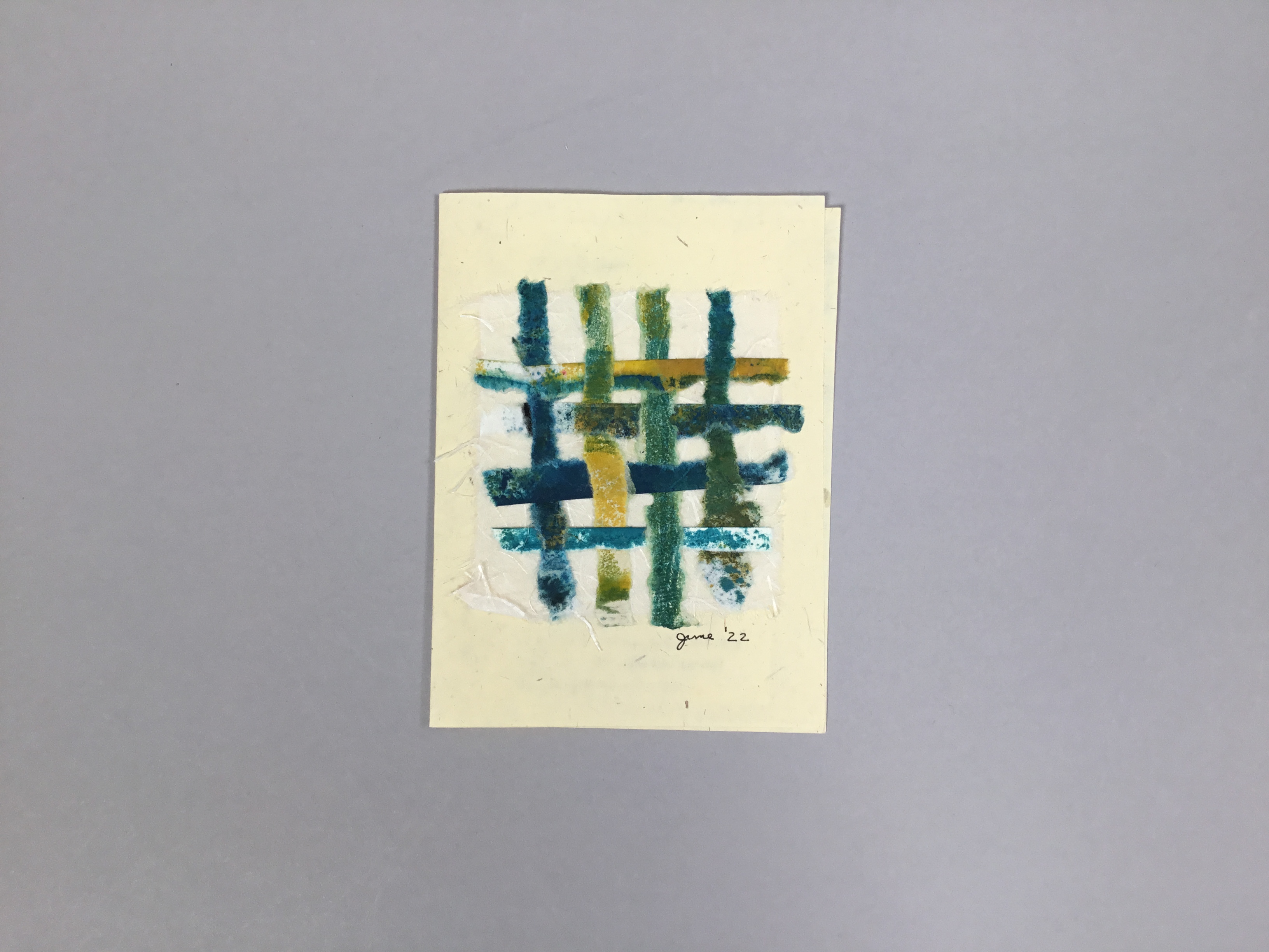 This card-like piece is made of a pale yellow Costa Rican lemon paper with a square piece of interwoven white, blue, yellow, and green scraps of paper on the front. 