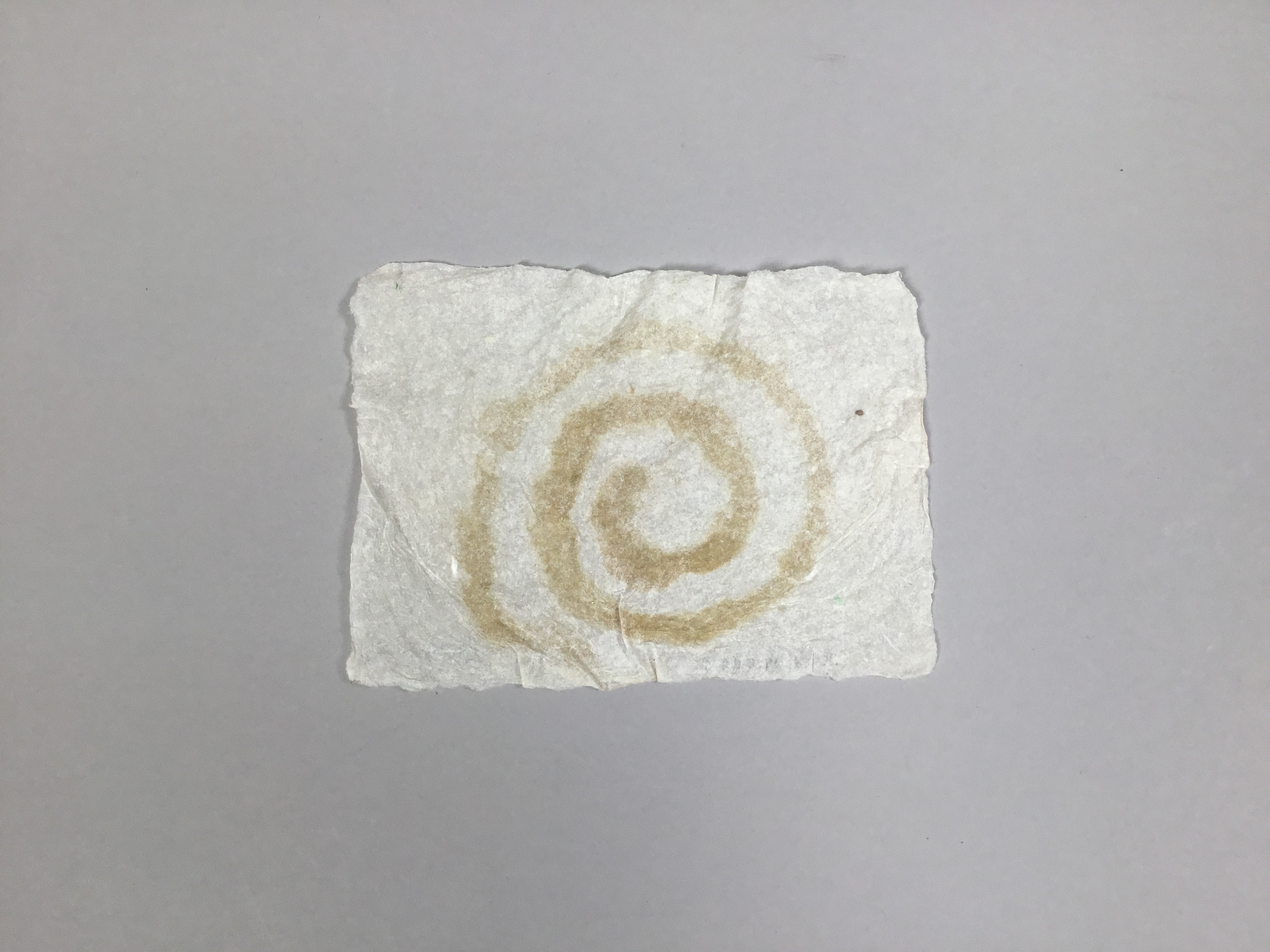 A square sheet of grey near-translucent handmade paper with a light brown counter-clockwise spiral.