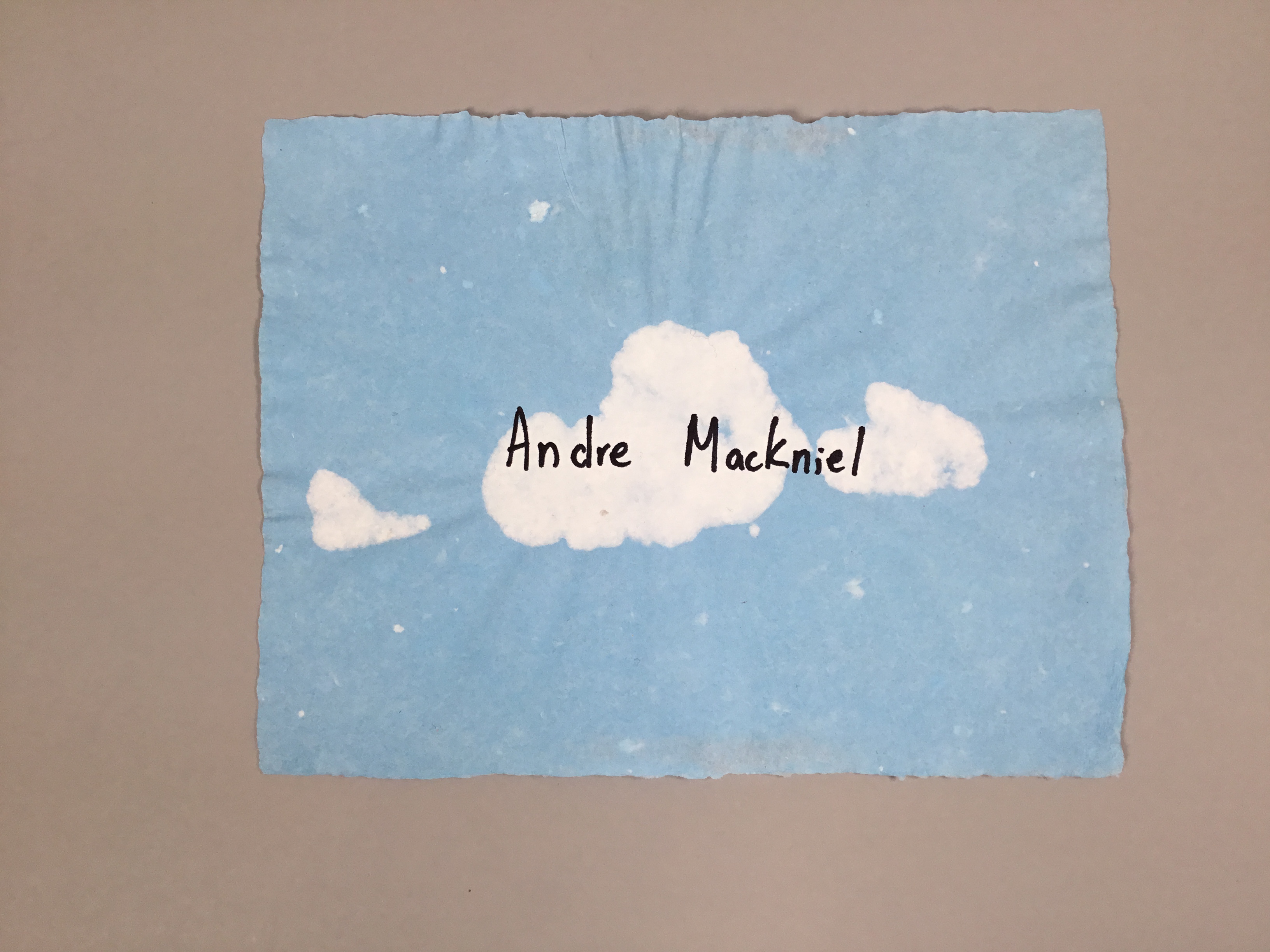 This piece is a rectangular piece of sky-blue paper with white clouds in the center. Andre Mackniel's name is written on the clouds; he was one of the ten victims of the Buffalo shootings in May of 2022.