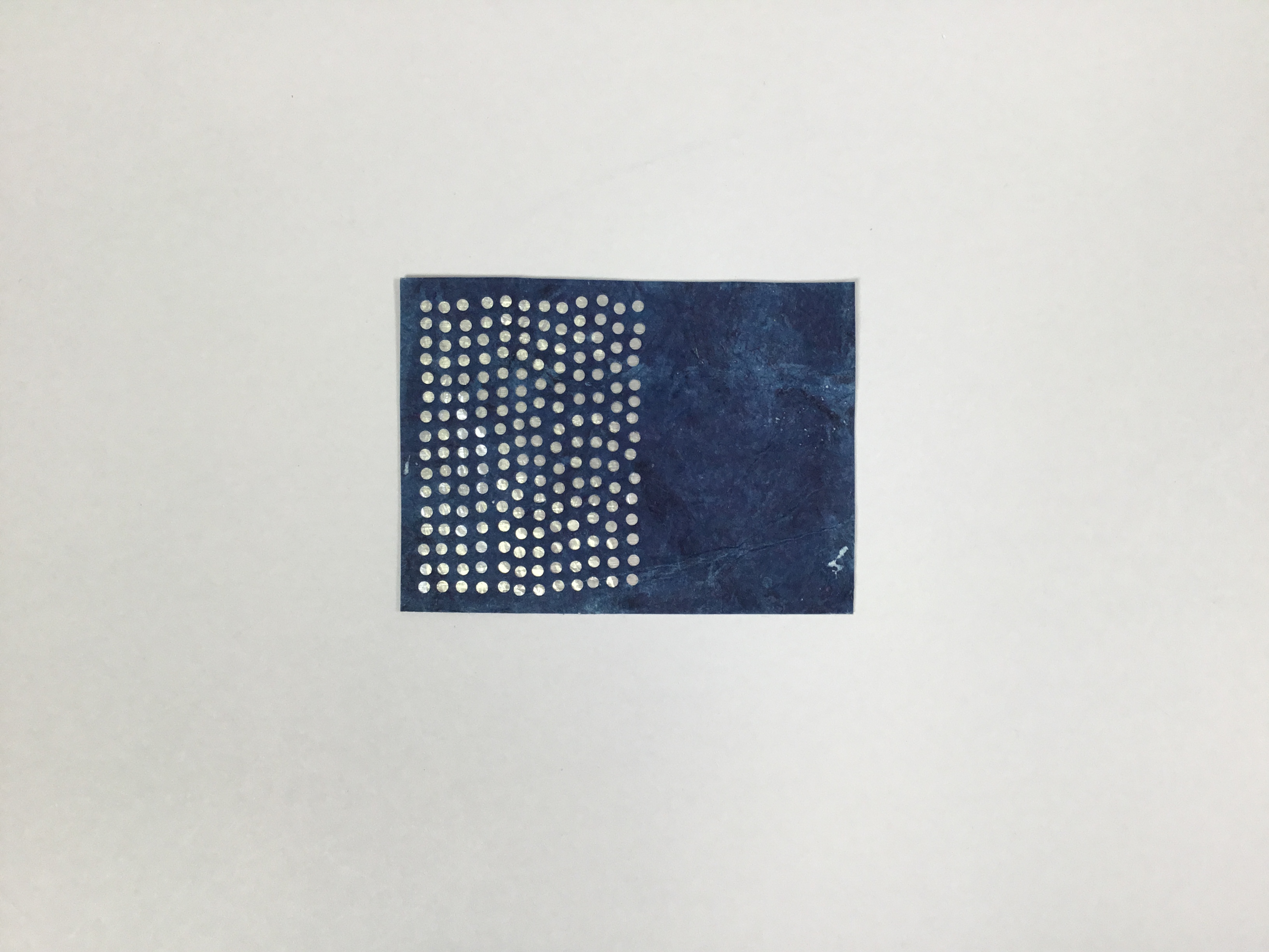 This piece is a rectangular, dual-layered sheet of paper. The top layer is a deep blue with circular perforations on the lefthand side. The perforations reveal the bottom layer, which is tin foil.