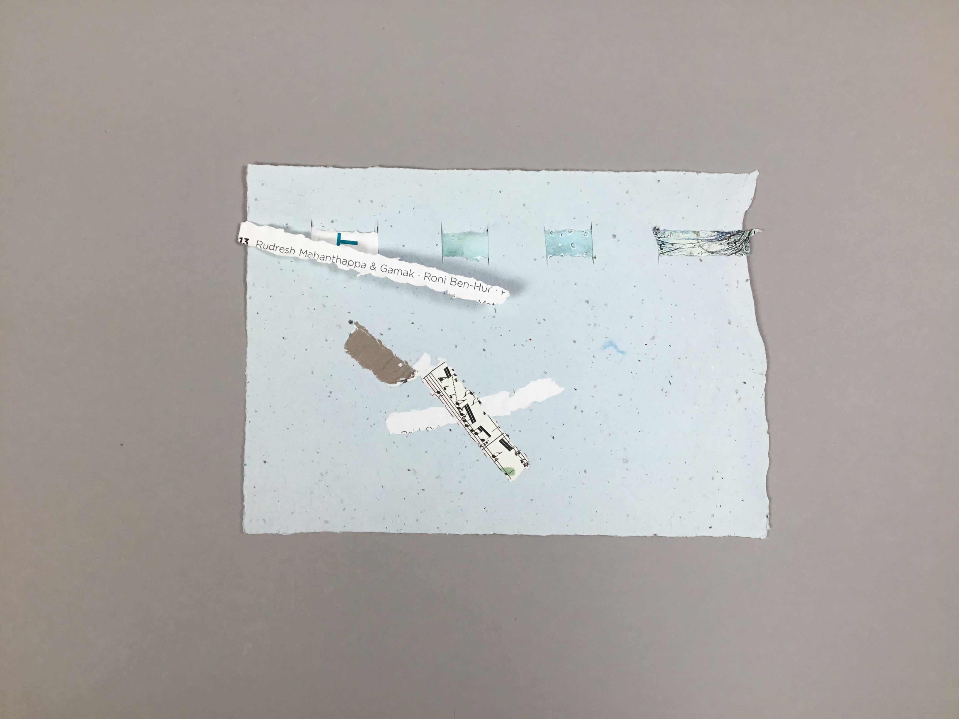 This piece has a lightly speckled, eggshell blue background with scraps of concert program covers woven into the paper.