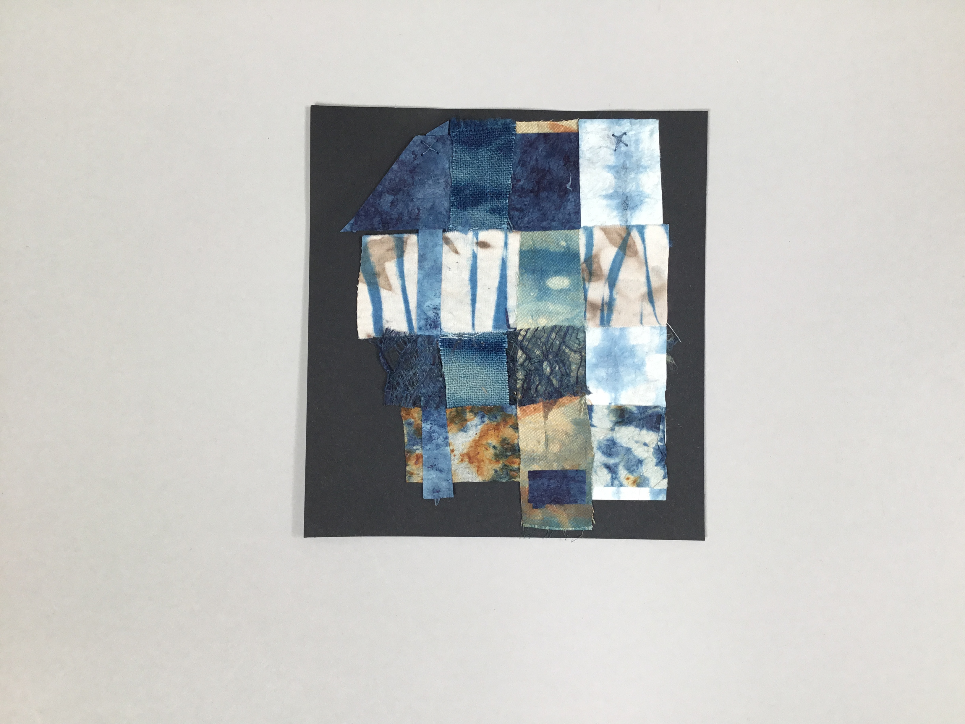 This piece is a collage of square blue scraps of fabric with varying patterns placed against a square, black background.