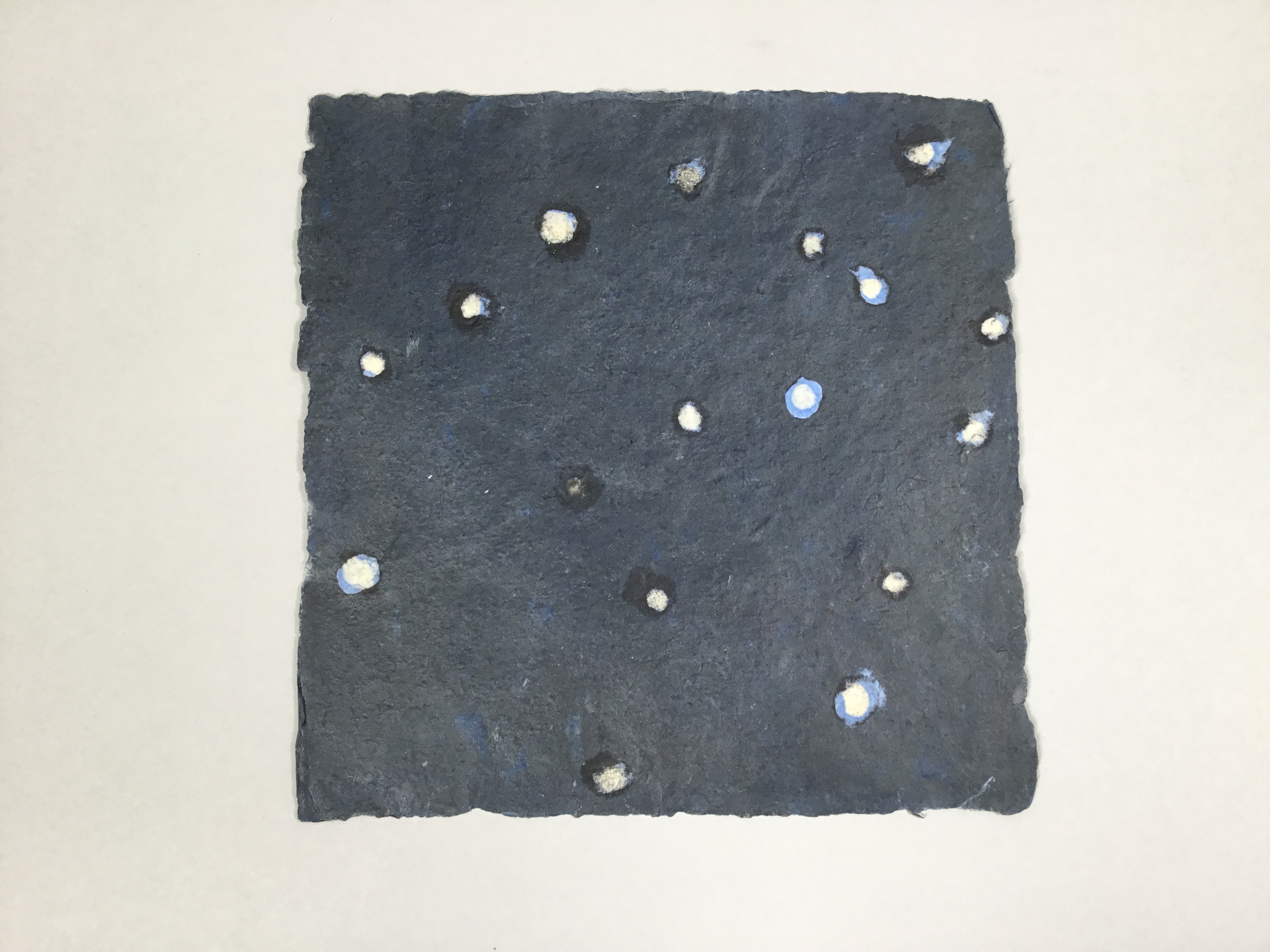 This piece is a square sheet of paper that is a mix of dark blue and black. There are white and light blue dots painted on top.