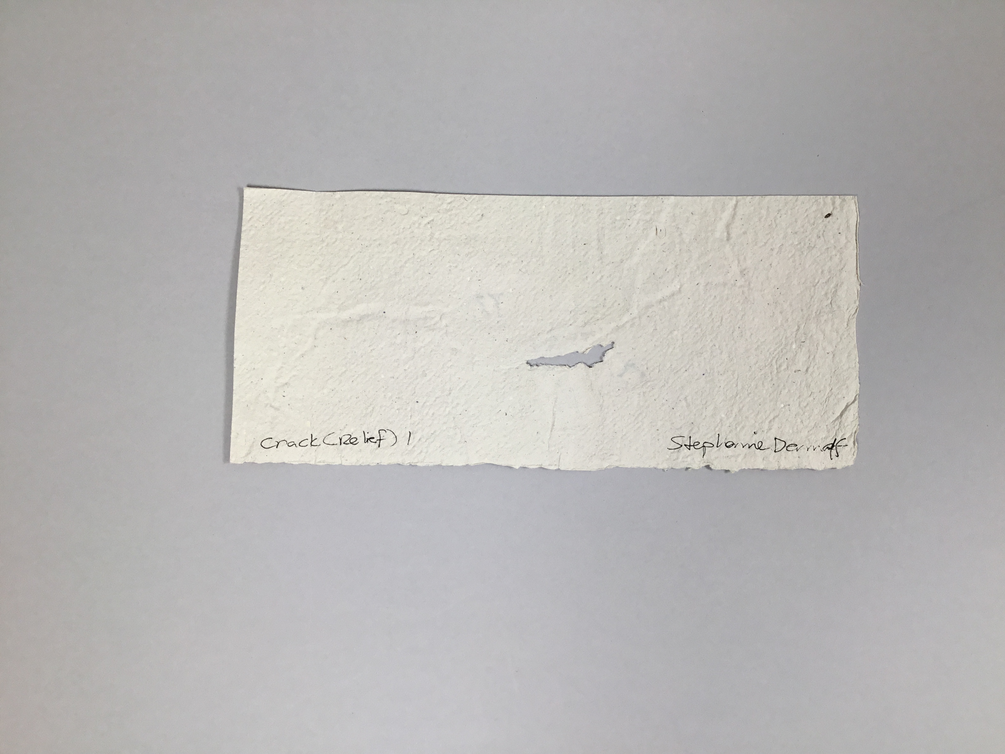 This piece is an off-white, slightly speckled and slightly textured sheet of paper with an intentional tear in the center. 