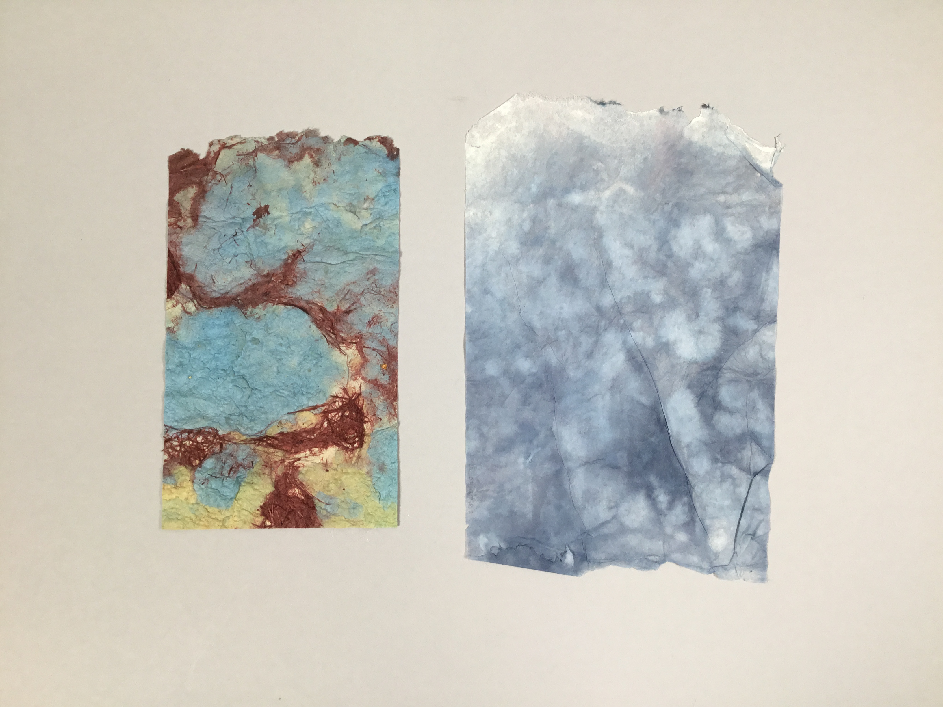 This piece is two separate sheets of paper. The one on the left is rectangular and has a brown, cyan, and mustard marbled pattern. The sheet on the right is slightly larger, and is varying shades of greyish blue and white, resembling a stormy sky.