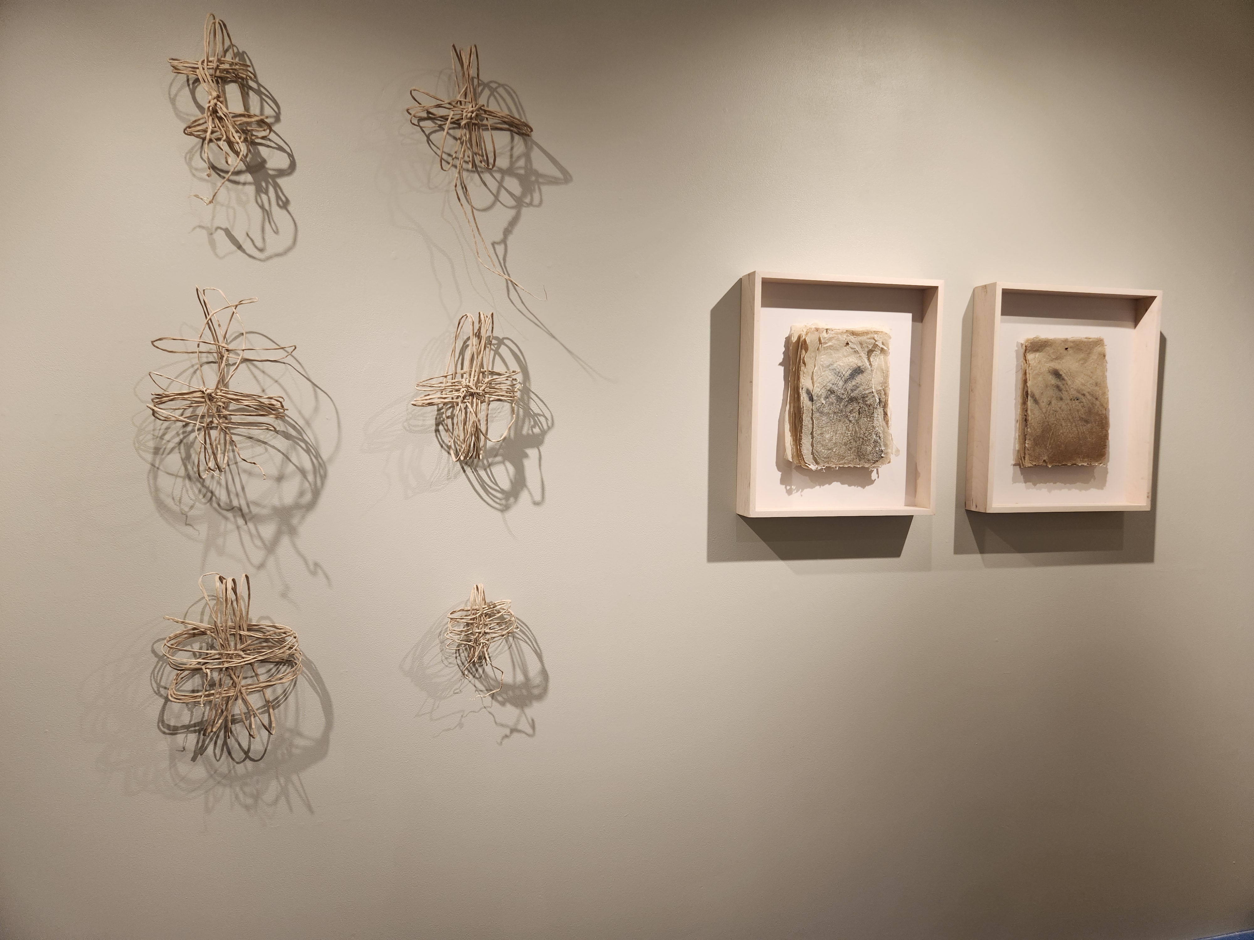 On the left, a collection of six tan lengths of abaca paper strings wound and knotted in various orientations. On the right, two framed stacks of paper with grass-like etchings.