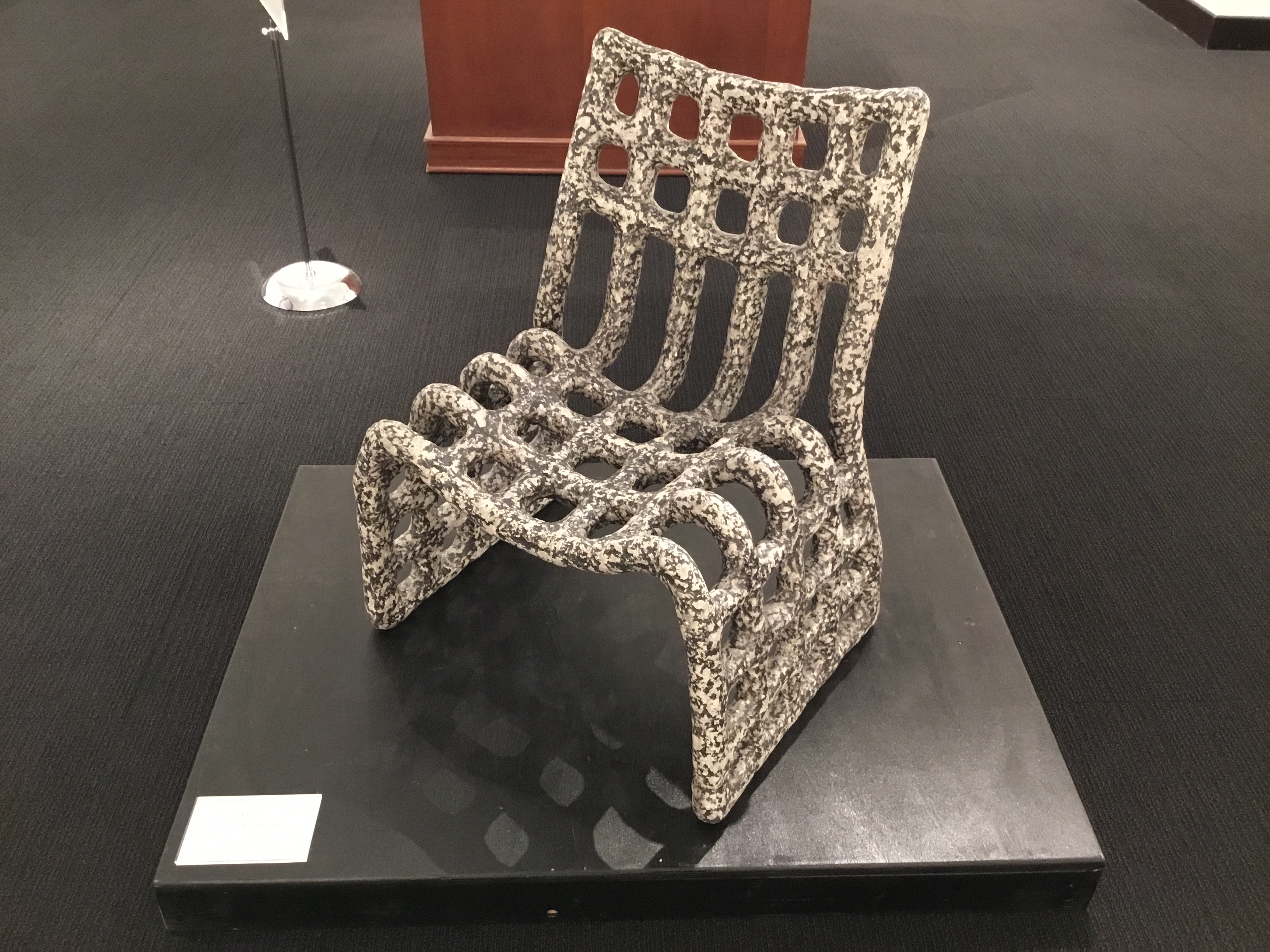 A closeup of an black and white speckled, waffle patterned chair with a curving seat, placed on a low black pedestal.