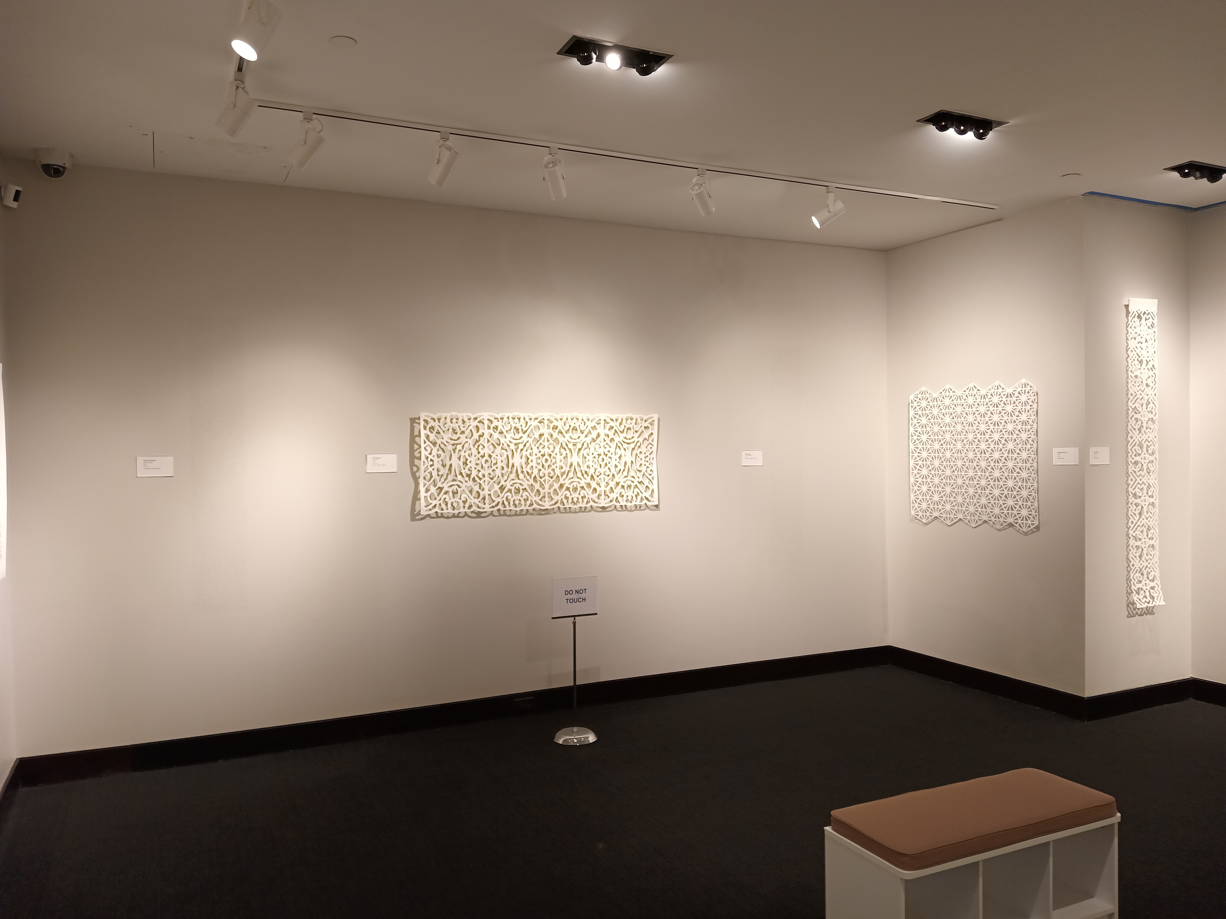 An overview of the front gallery. Along the walls are several intricate, geometric paper cuts on white paper of various sizes.
