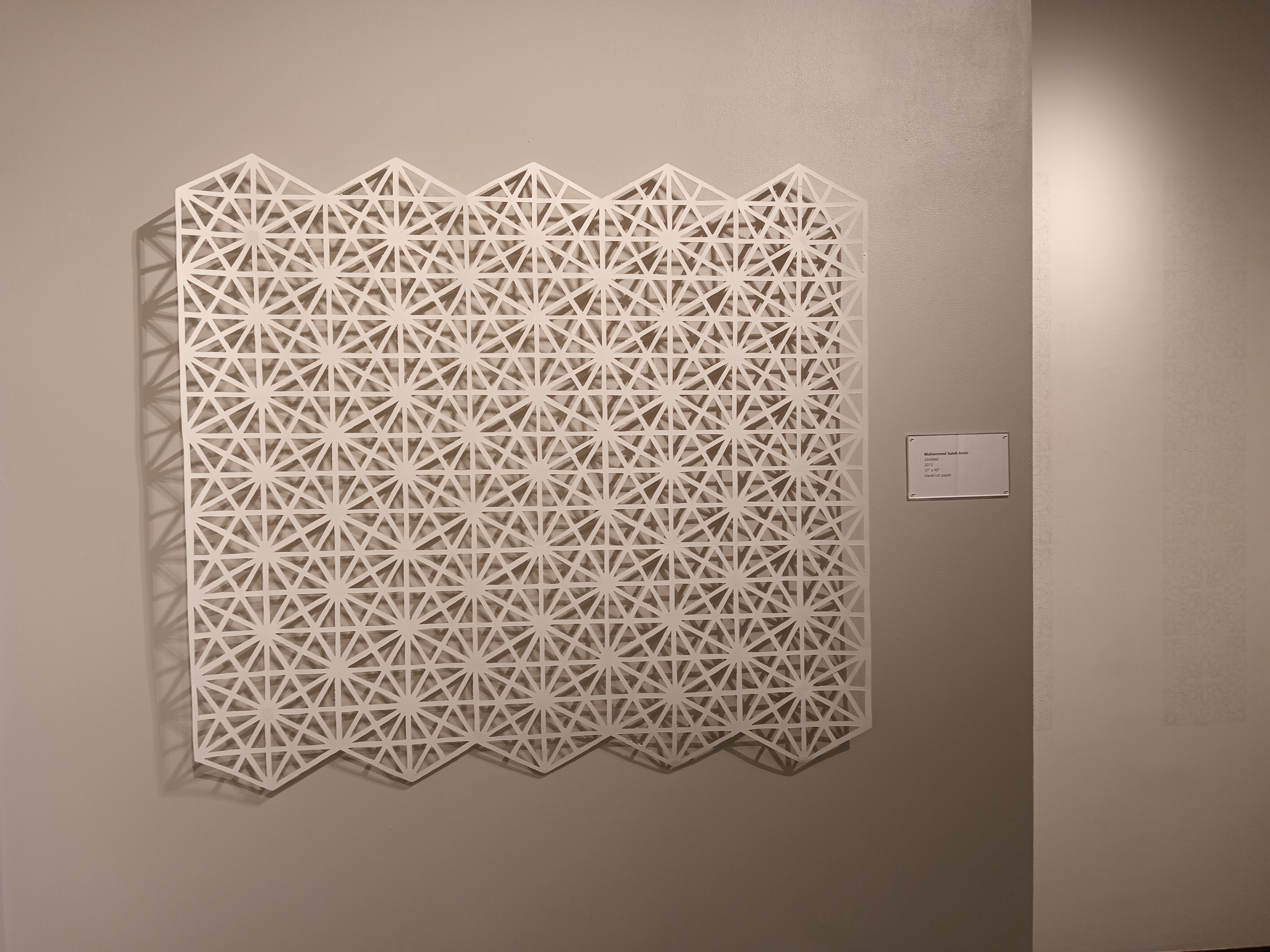 A view of a white rectangular paper cut artwork, featuring overlapping hexagons with lines radiating from their center points outward.