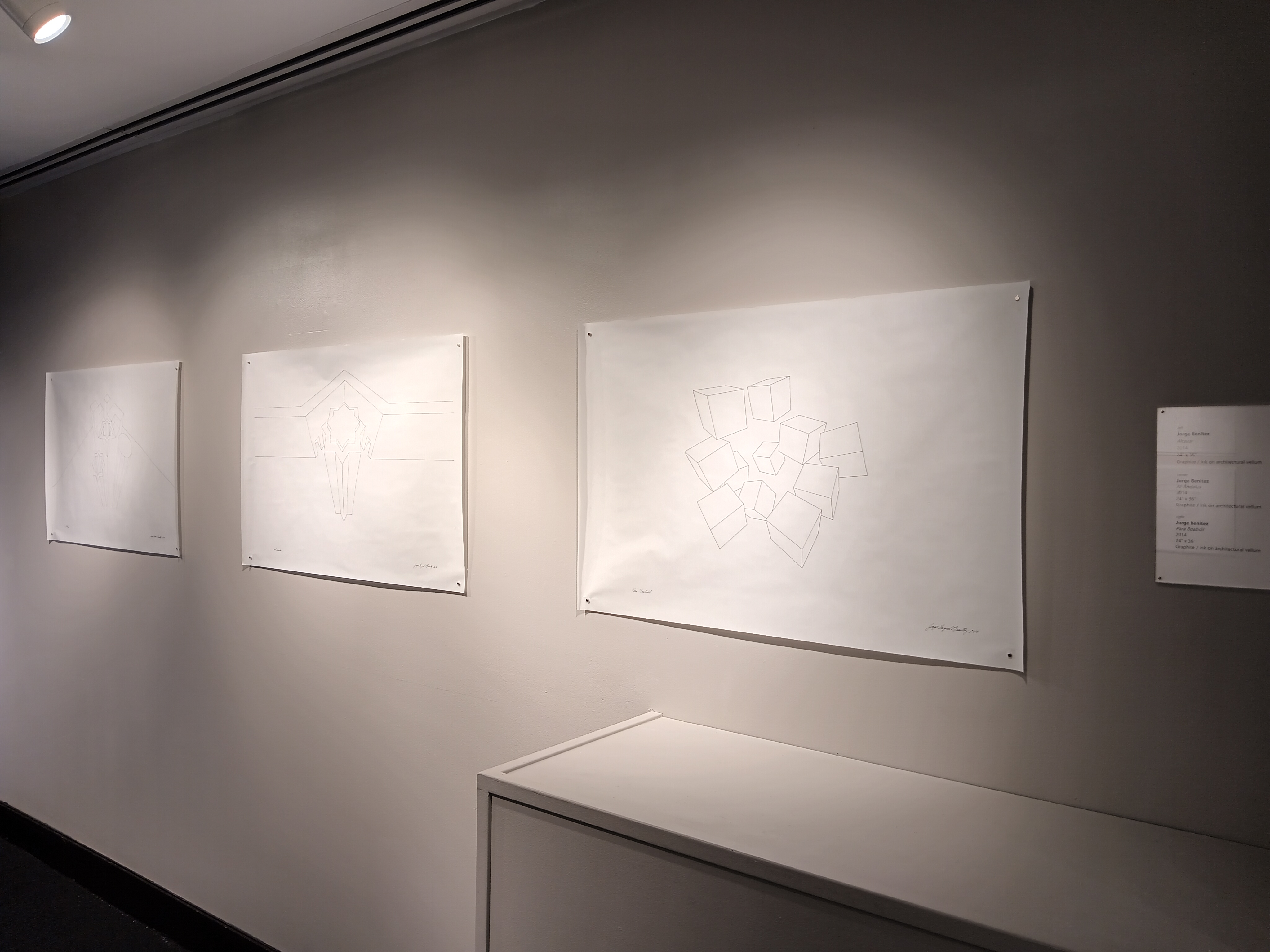 A view of three graphite drawings on white paper, displayed in the back gallery. In the foreground is a perspective drawing of several cubes floating in space.