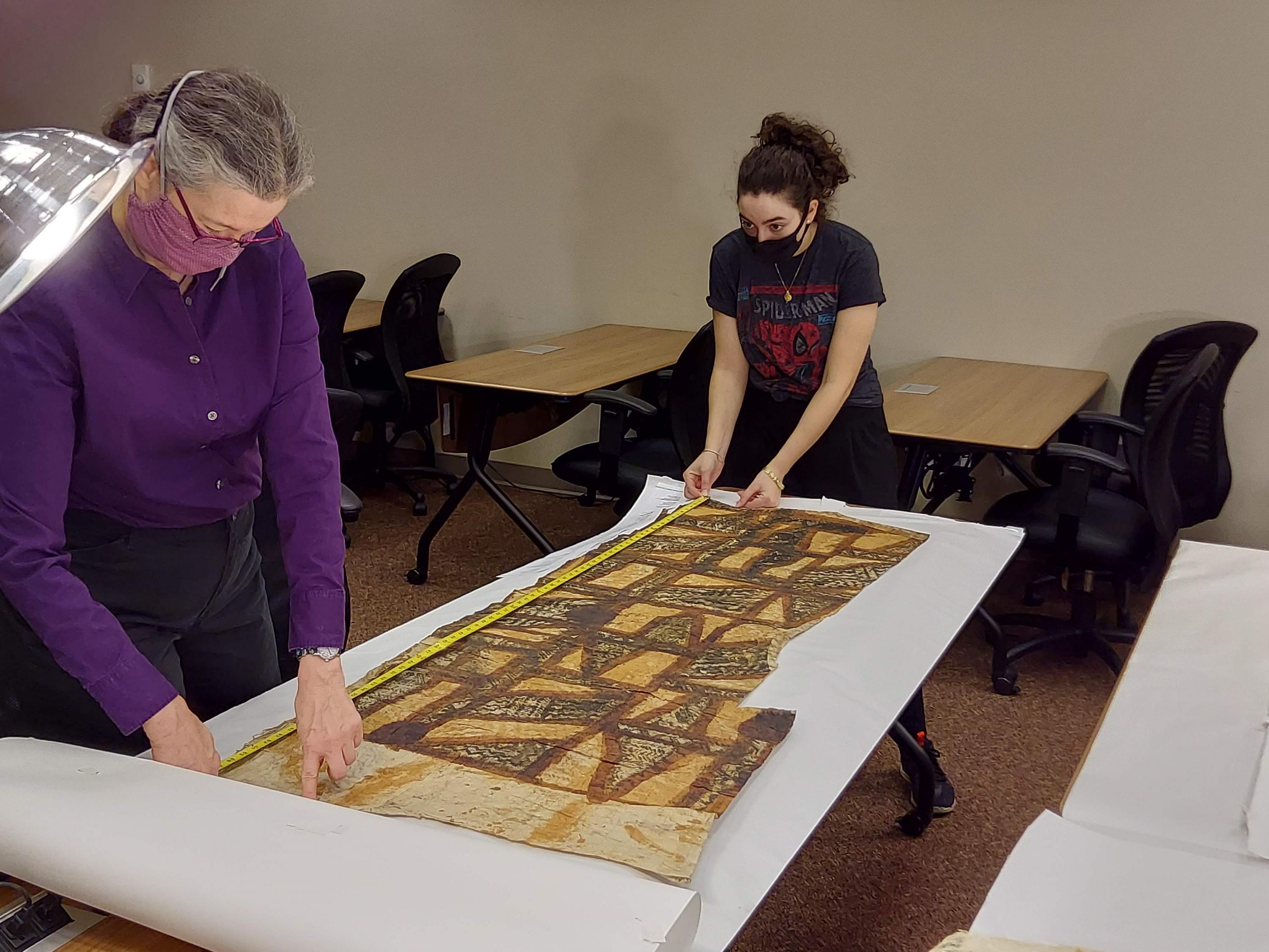 Conservator Stephanie Watkins closely examines a large example of Tapa Cloth, while undergraduate Teresa Munoz assists. 