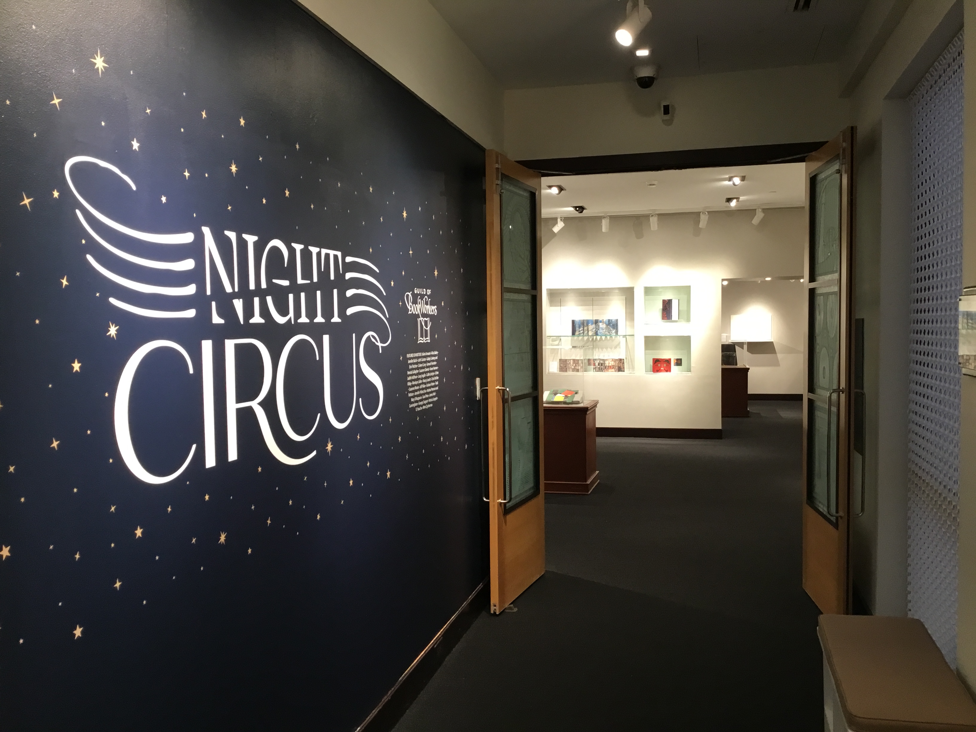 Photo of the entryway to Night Circus. The title Night Circus, on a deep blue background, is surrounded by tiny stars and the double doors to the right are open to the exhibit.