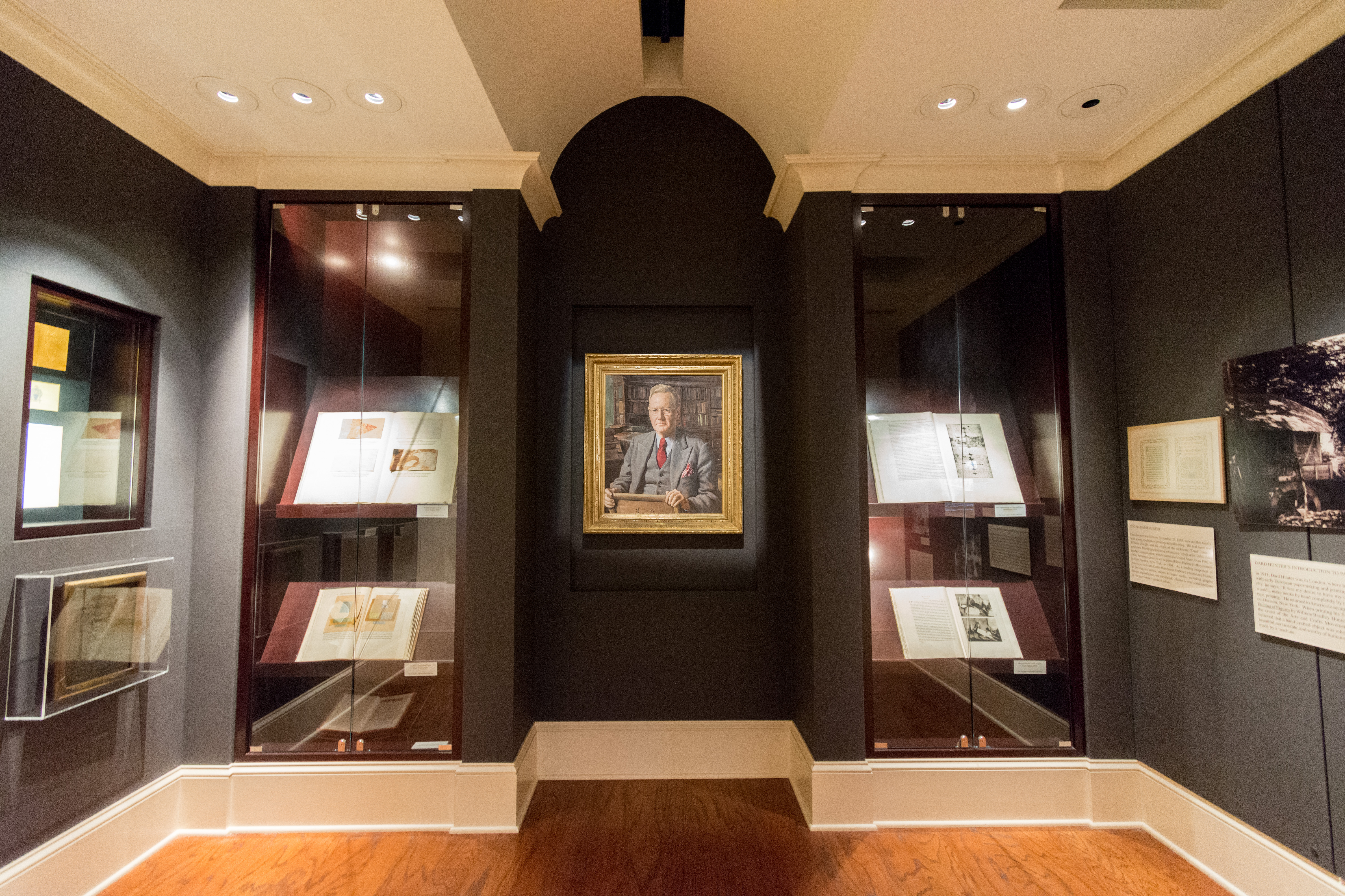 The Dard Hunter Gallery centers a portrait of the Paper Museum founder. On either side of the painted portrait are cases housing handmade books written, typeset, and printed by Dard Hunter.