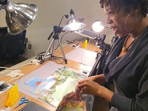 African American woman standing in front an animation station with clamp lights and a magazine collage background