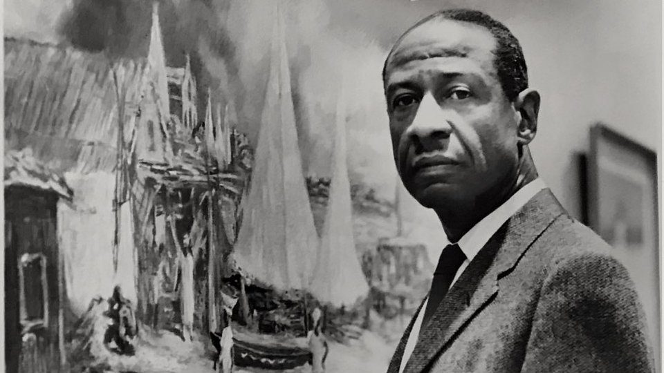 Black and white photo of James A Porter, an African American man in a suit looks directly at the camera while standing in front of a giant painting