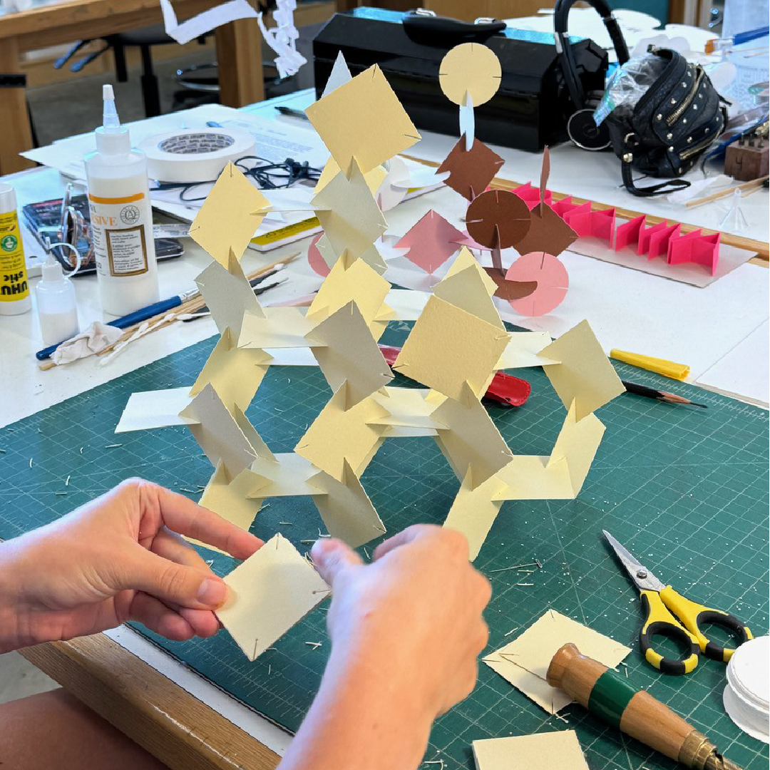 A pair of hands assembles a paper sculpture.