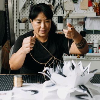 Artist Colette Fu in her studio pulling strings of a pop up constructions