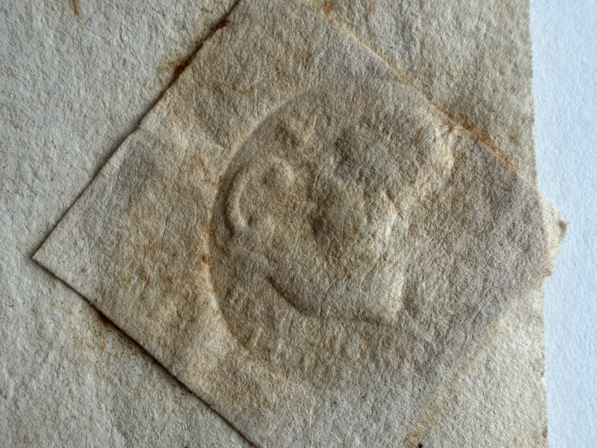 Close up shot of slightly aged embossed seal on tan paper. The seal looks like a man with a curled hook