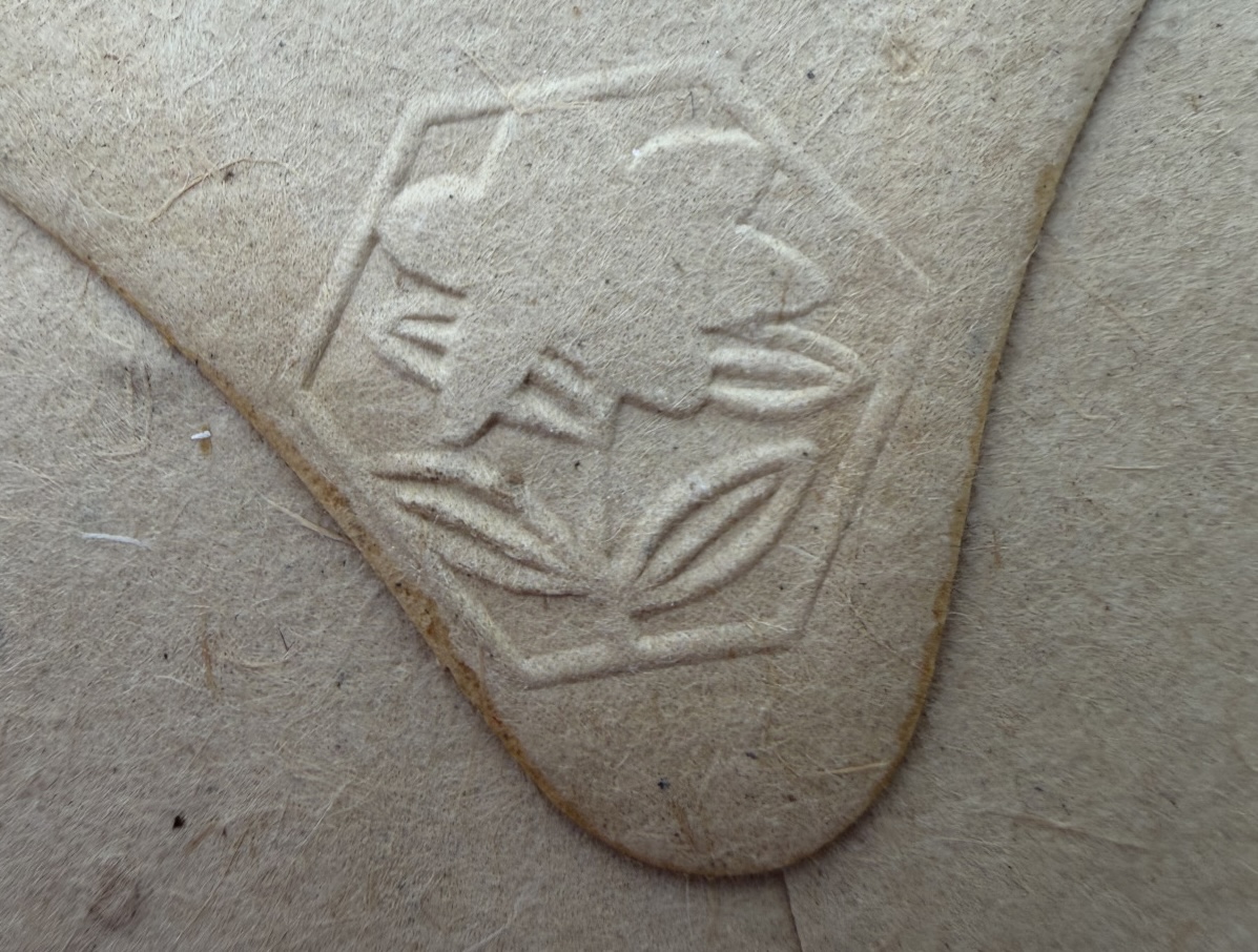 Mid distance shot of a beige envelope with small bits of bark and an embossed flower.