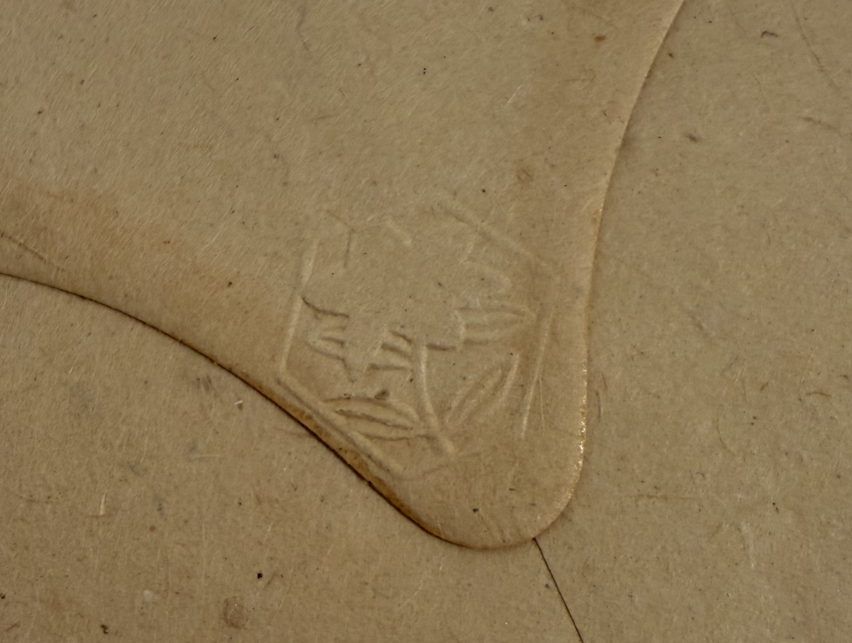 Close up detail shot of a beige envelope with small bits of bark and an embossed flower.