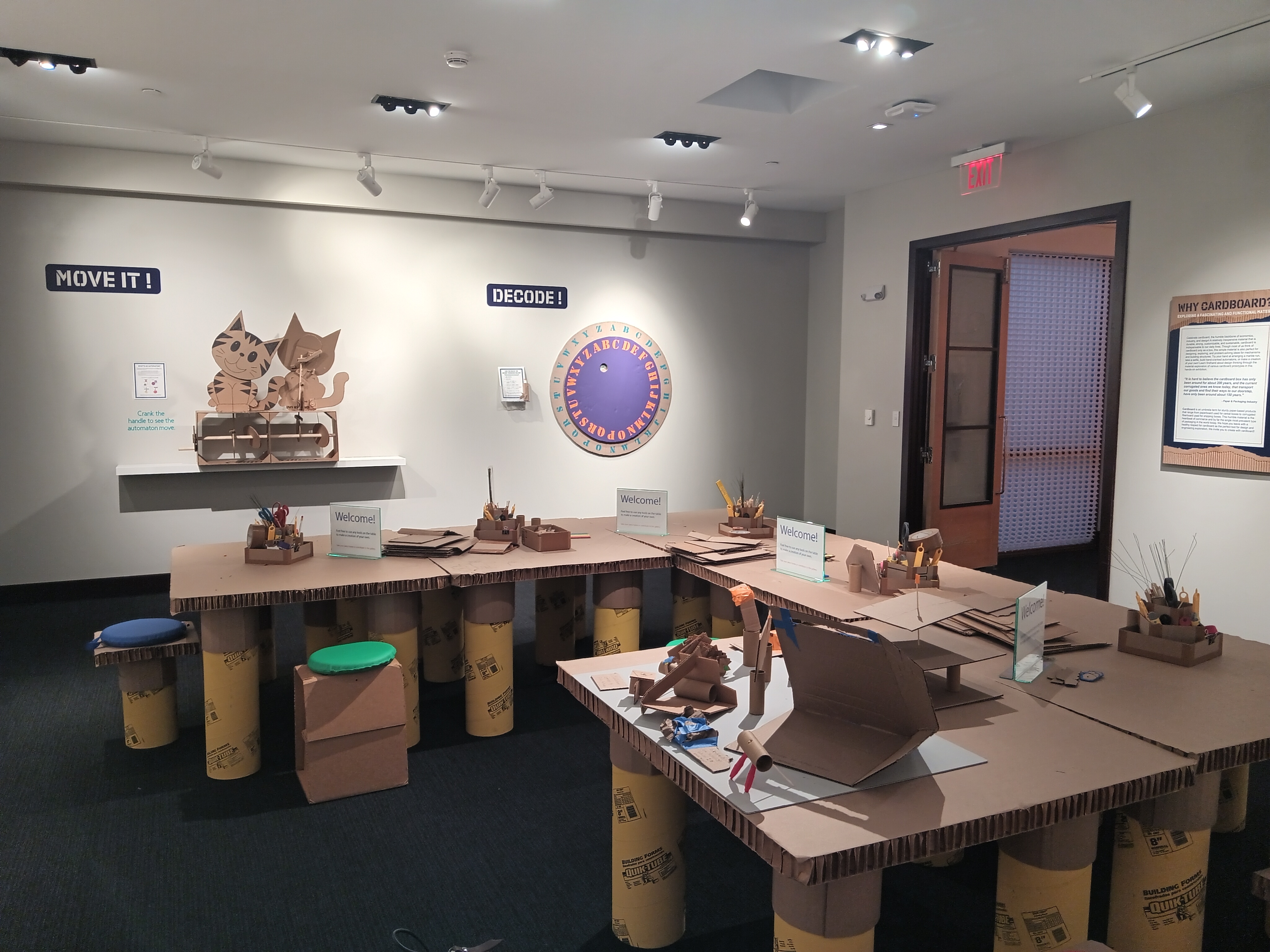 Overall view of the front gallery. In the foreground are cardboard tables, chairs, and various materials for guests to craft cardboard creations.