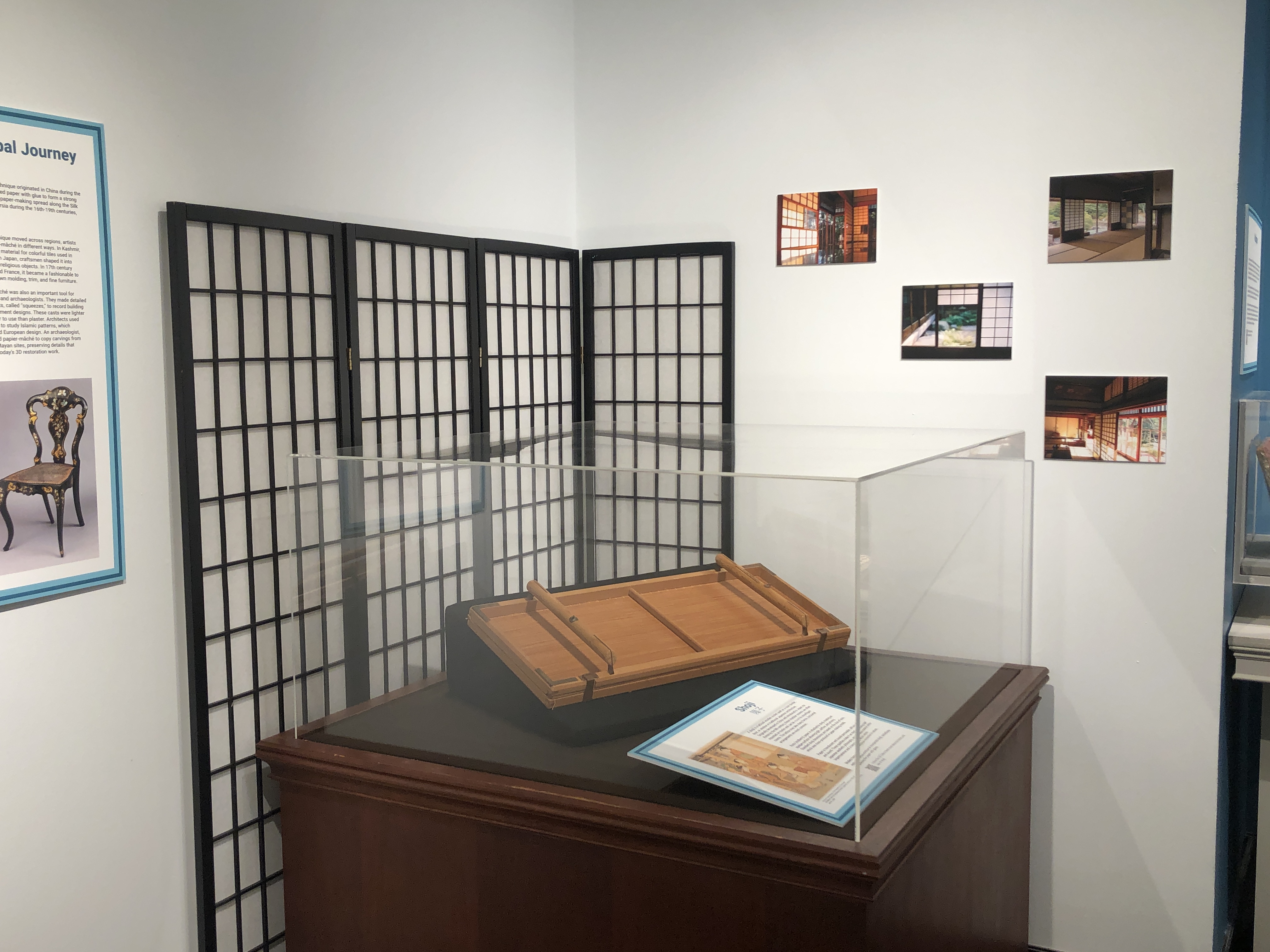 A display case housing a shoji mold sits in front of full sized a shoji screen; to the right are a series of photographs of shoji screens.