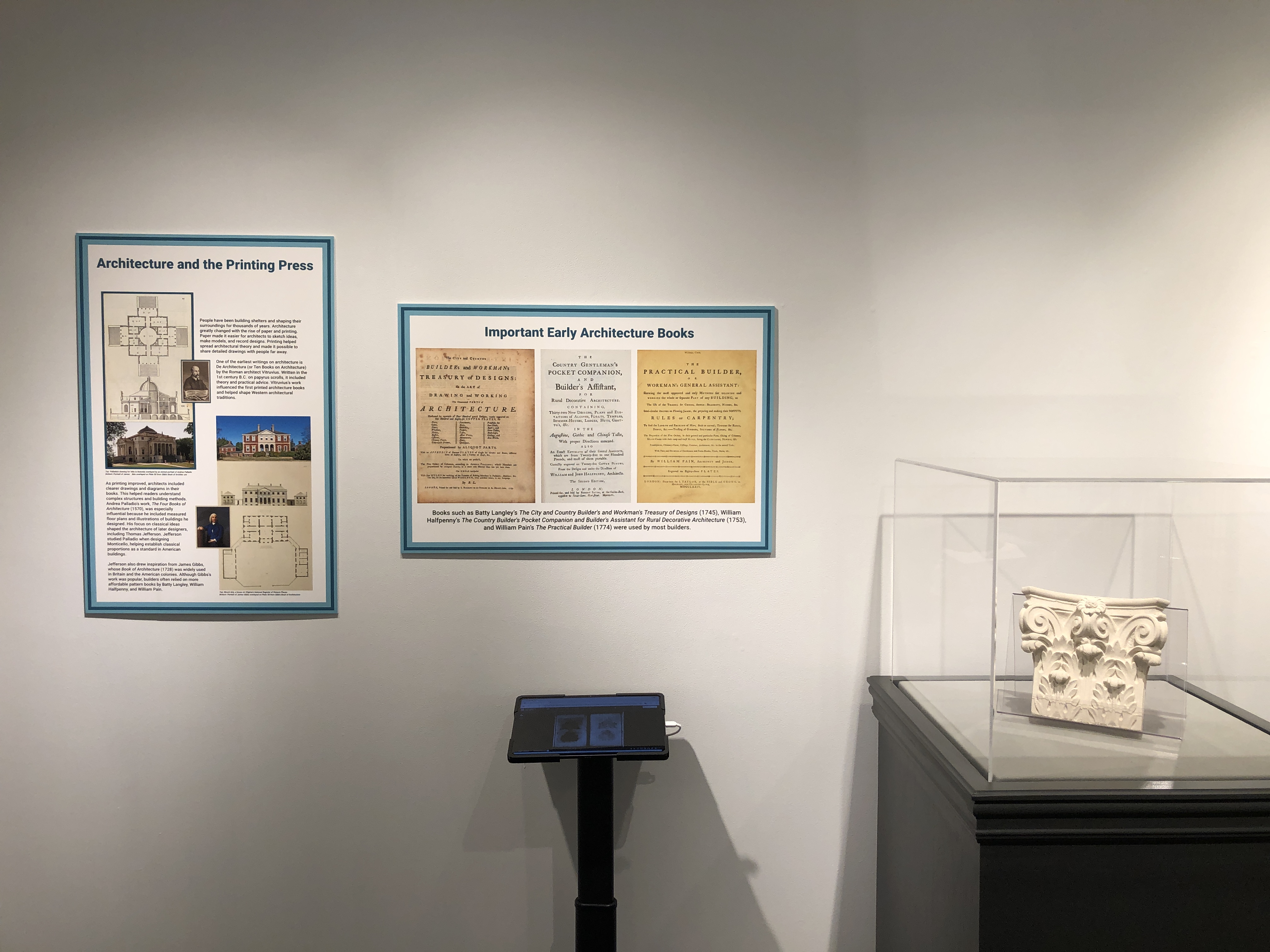 A view of two exhibition boards, a tablet, and a display case housing a model Doric column. 