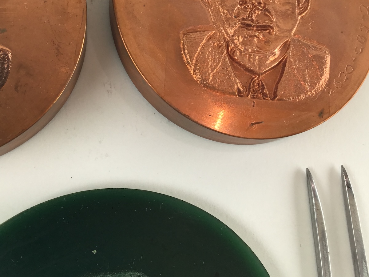 Two copper embossing plates above a dark green silicon mold on a white background. To the right of the plates are the four thin tools used to carve, two silver metal and two wooden sticks.