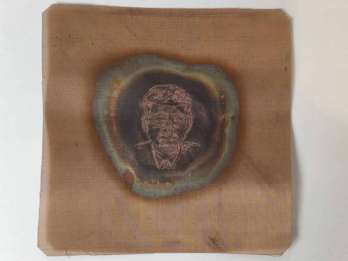 Copper colored sheet with an embossed image of JFK’s face and shoulders.