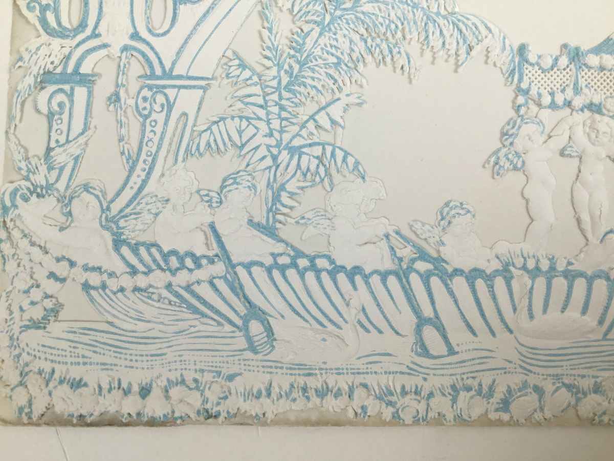 Close up of a blue and white greeting card that shows plants, water, and cherubs flying and rowing the boat.