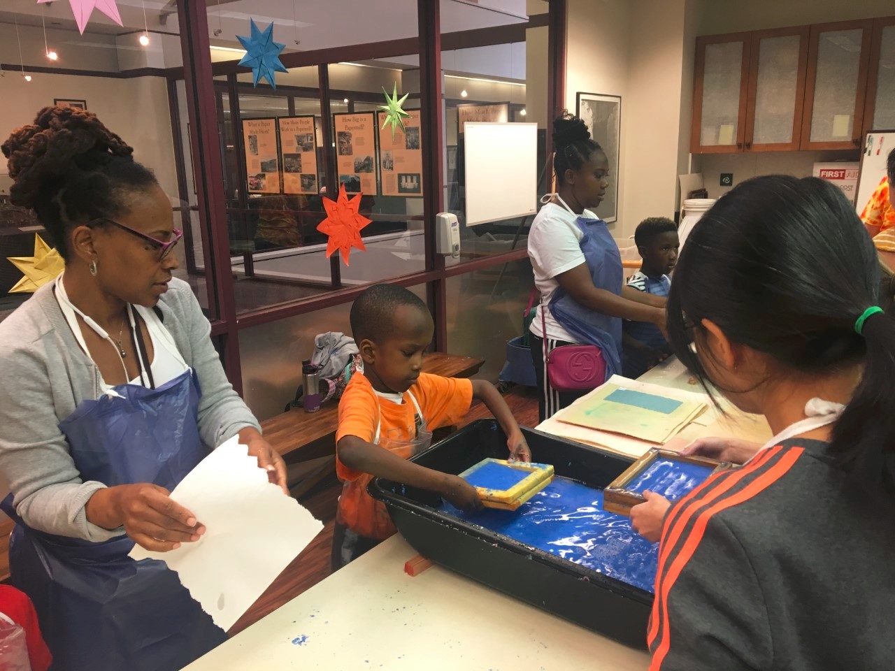 Young boy scooping blue paper pulp out of a vat with his mould and deckle during a workshop in the Paper Museum classroom.