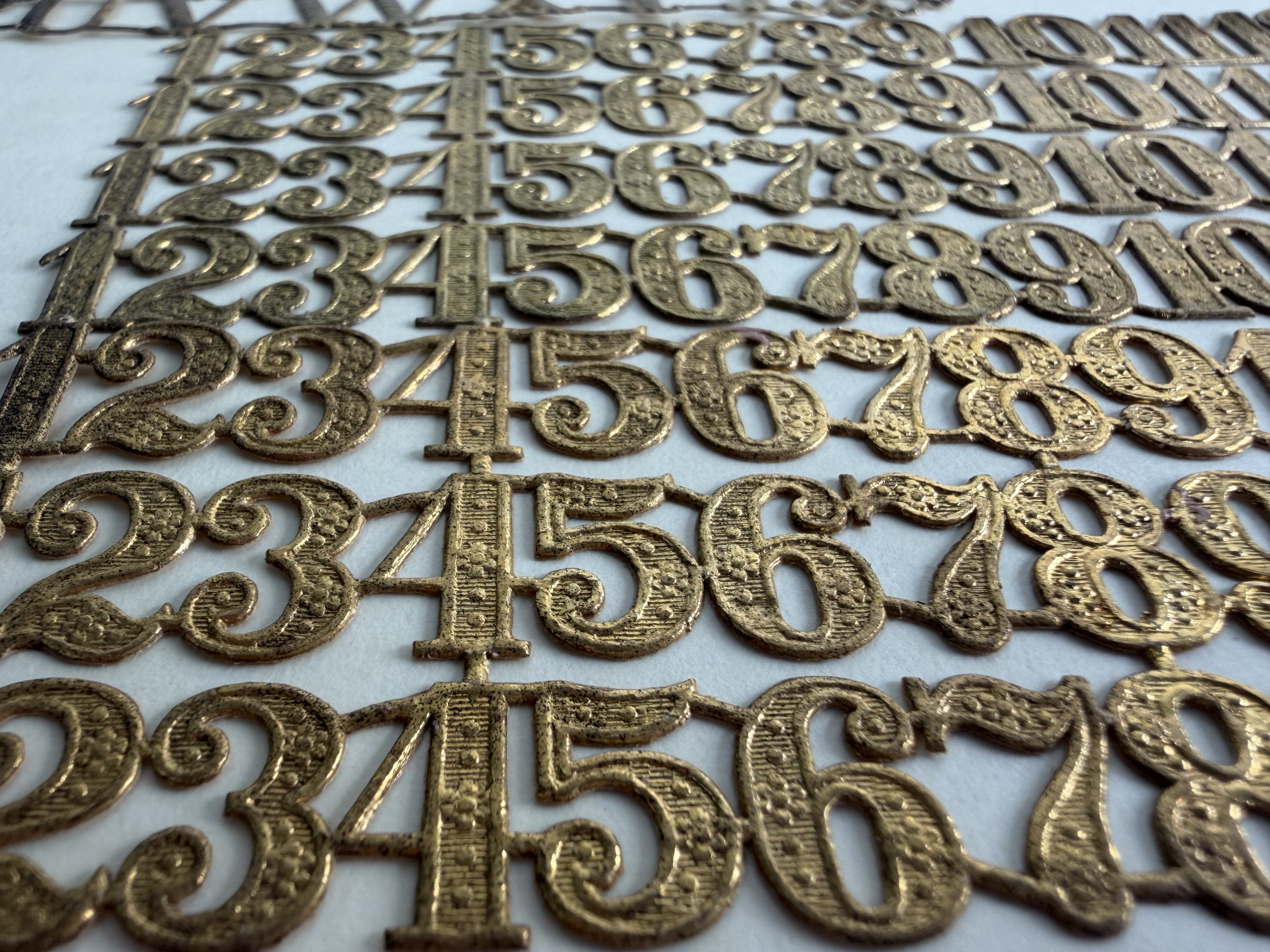 Bronze colored paper shaped like numbers 1-10 on white background. They are attached to each other in straight horizontal lines.