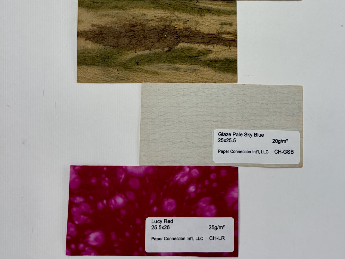 Three rectangular strips of paper, with one being white, another purple, and another camouflage.